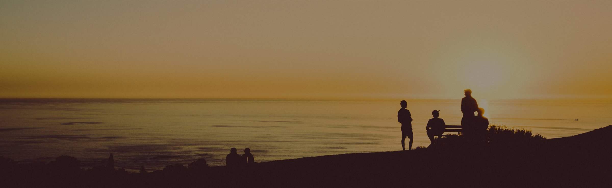 people outdoors on a beach near the ocean while sun is setting