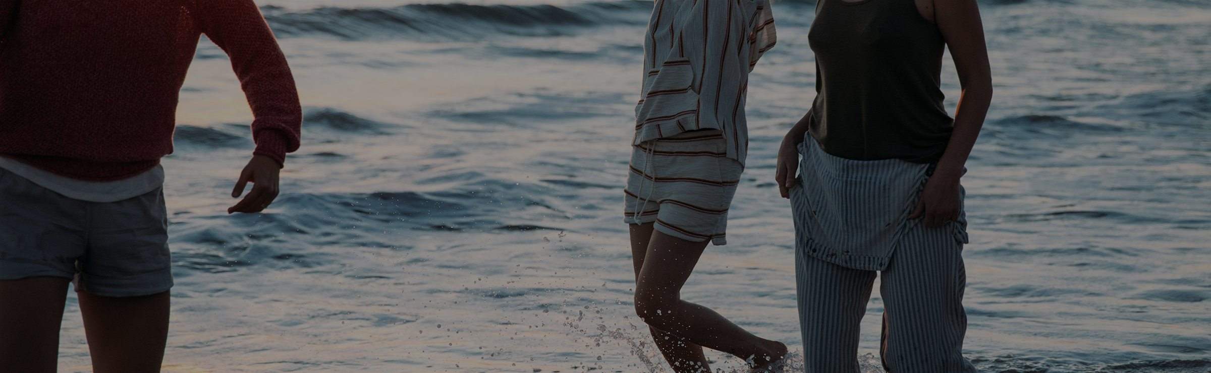 A woman walks over coastal rocks in a sweater and pants.