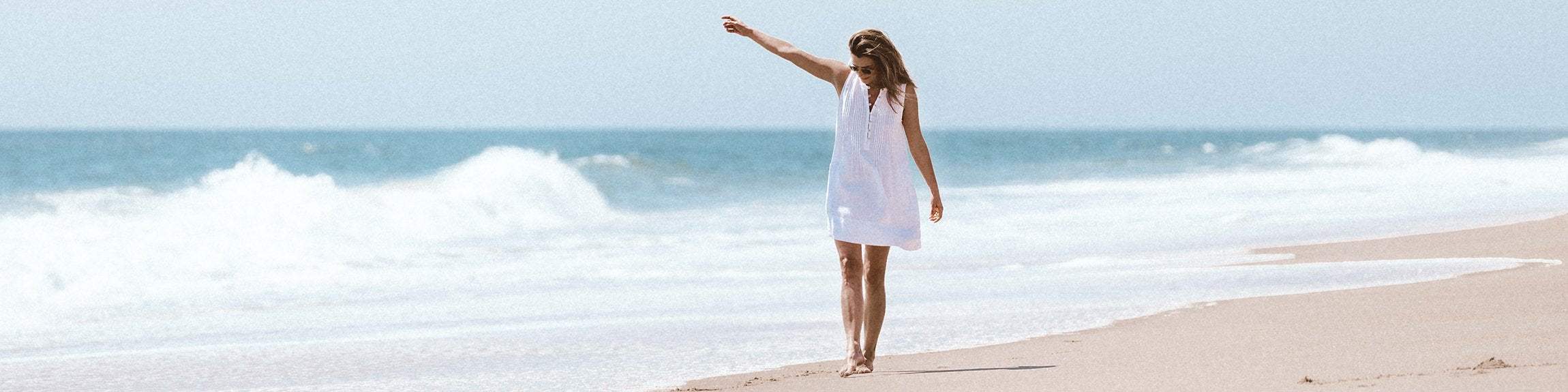 woman in a white sleeveless dress walking on the beach