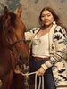 Bethany Yellowtail in a patterned duster with a horse in the foothills.