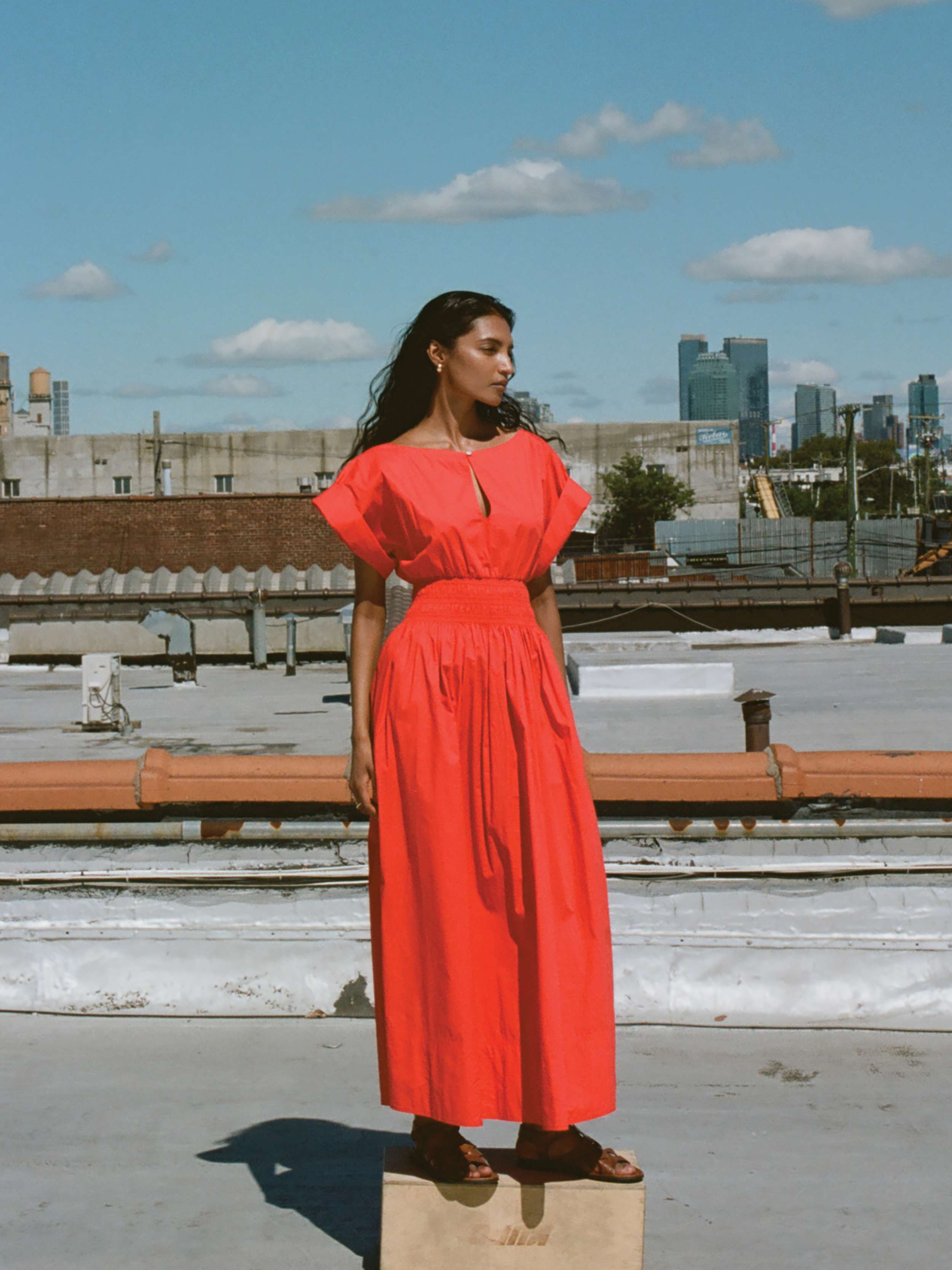 Woman wearing a short sleeve red dress standing on a wooden block on a rooftop