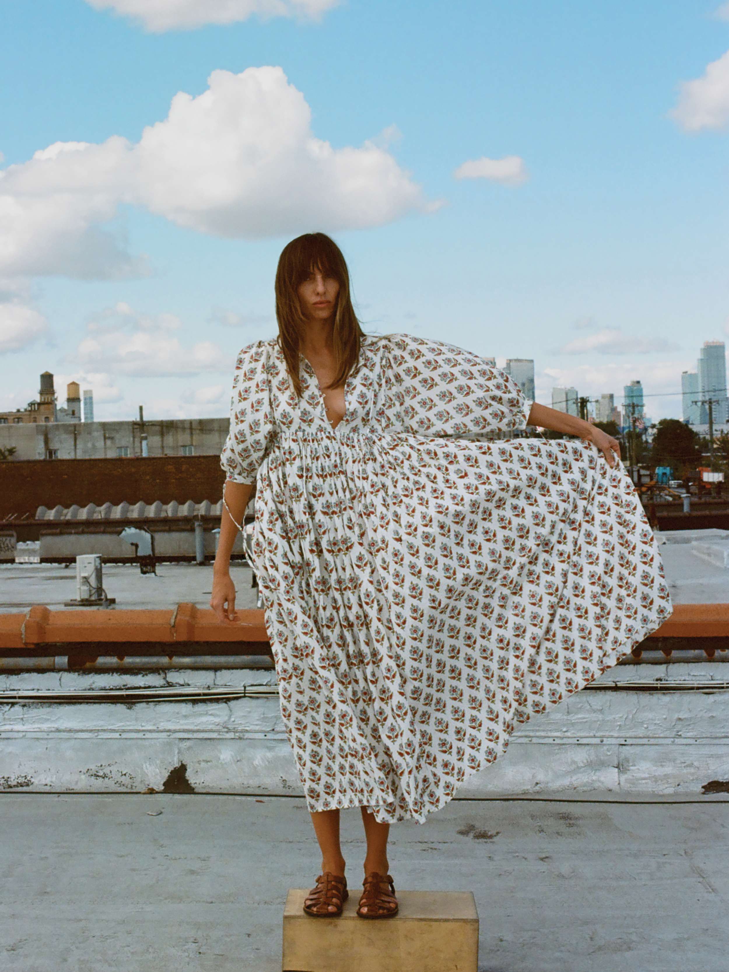 Woman in a patterned dress standing on a rooftop with a cityscape in the background