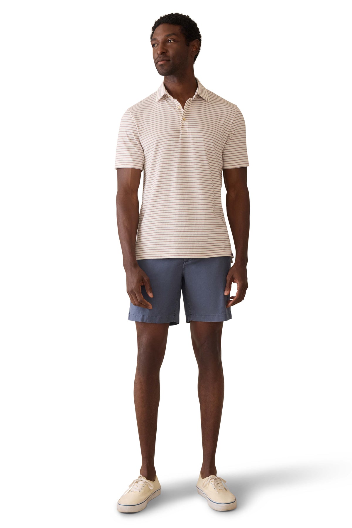 A man wearing a striped polo shirt, blue shorts, and sneakers, image 2 of 3