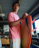 Man carrying a surfboard wearing a sunwashed t-shirt and shorelite shorts.