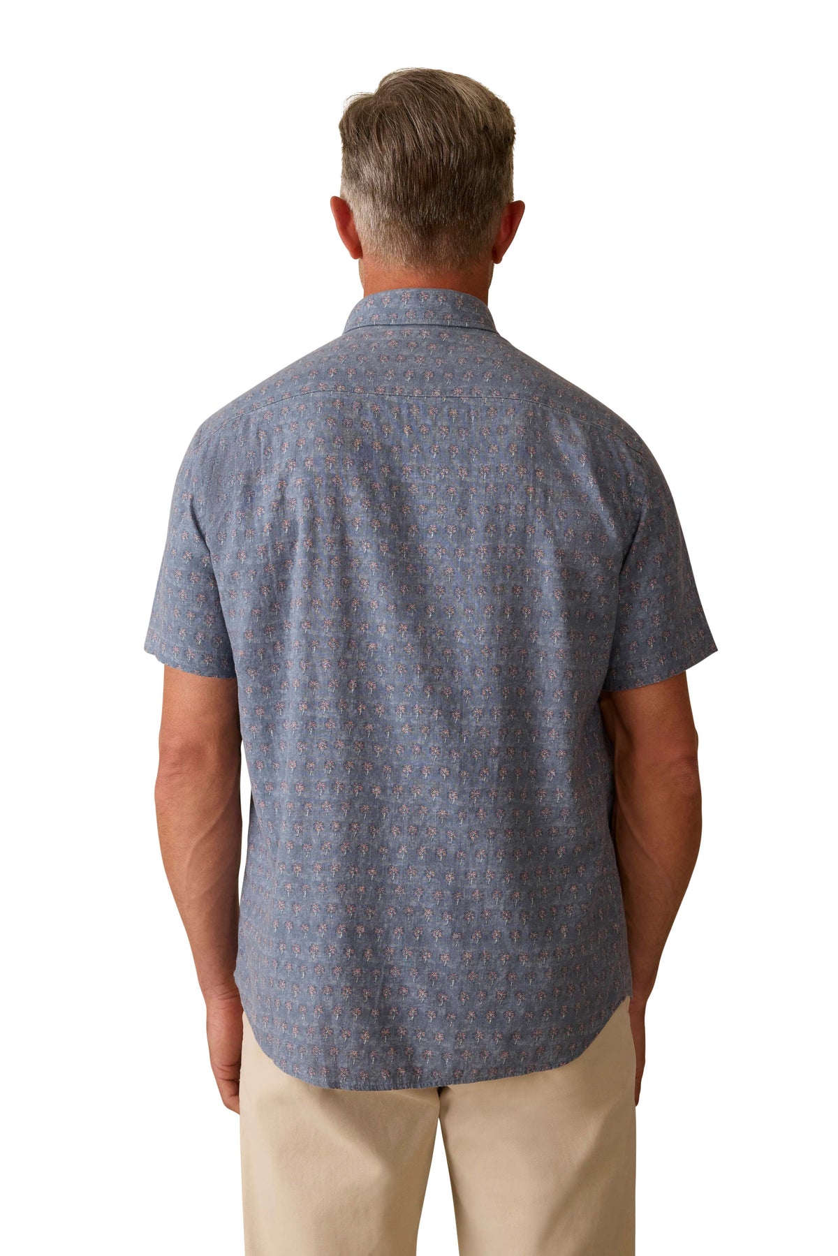 A man viewed from behind wearing a blue printed button down shirt and beige shorts, image 3 of 3