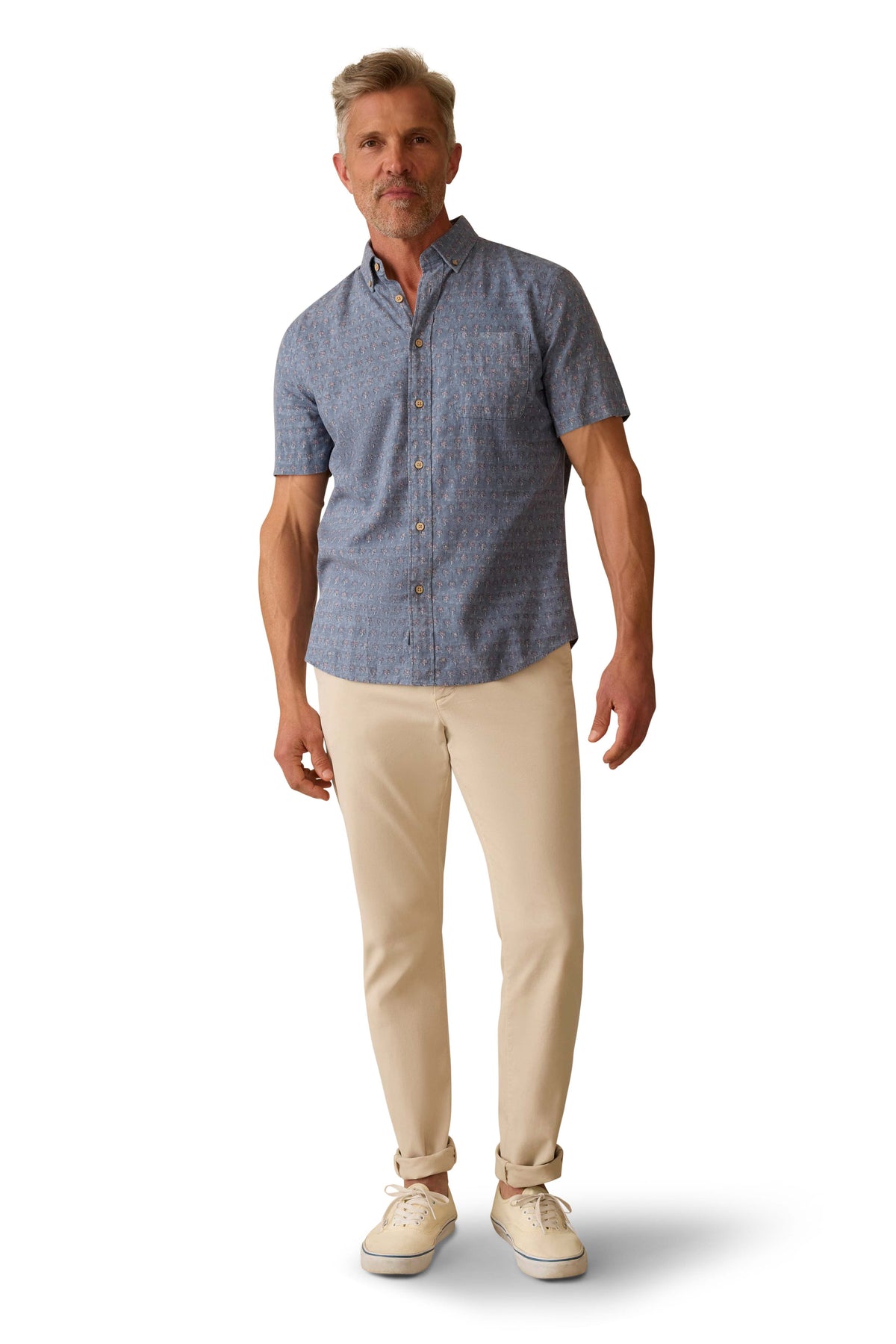 A man wearing a blue printed button down shirt, beige pants, and sneakers, image 2 of 3