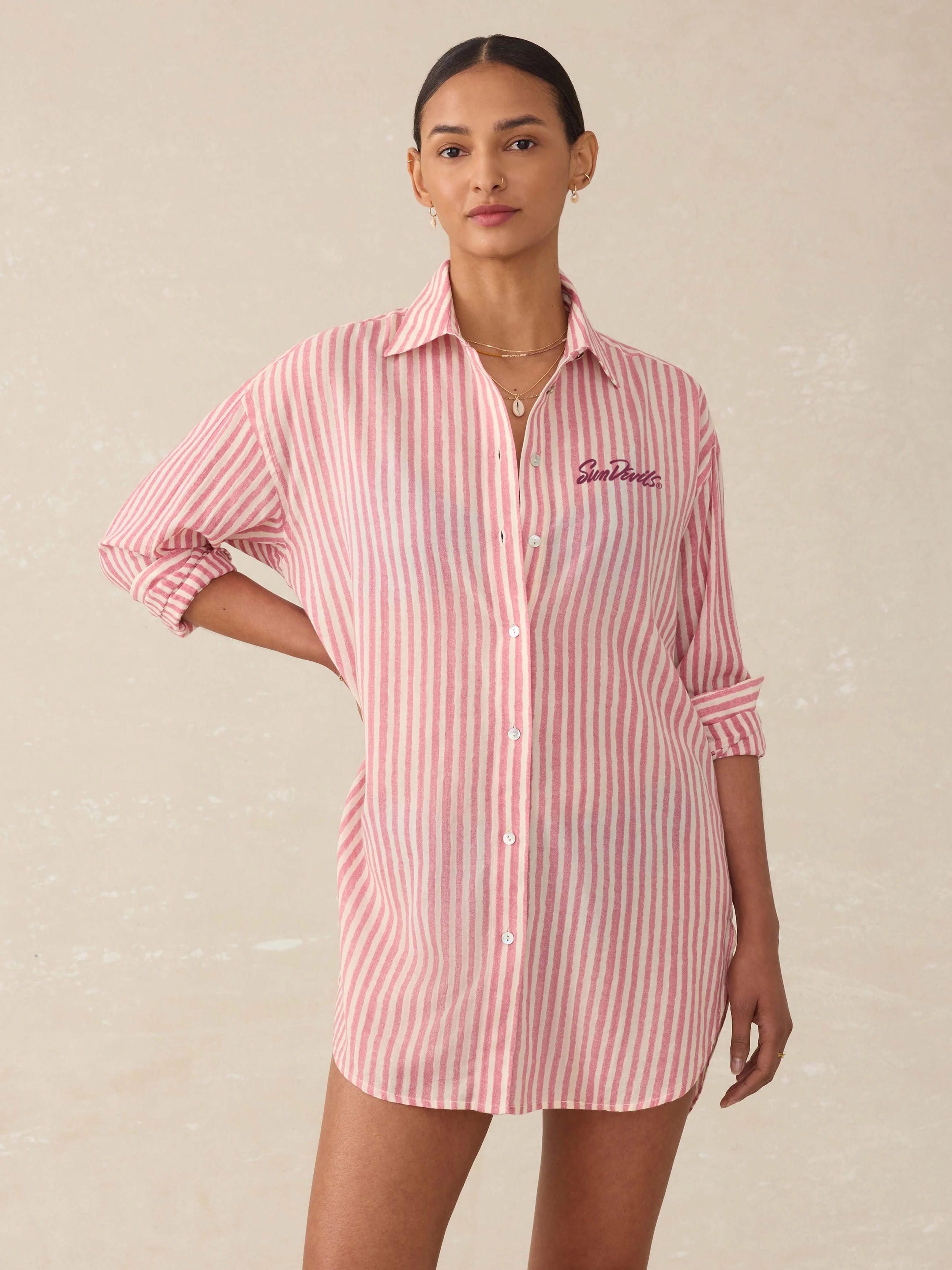 Woman wearing a pink and white striped shirt dress with Arizona State University graphic on the left chest against a beige background