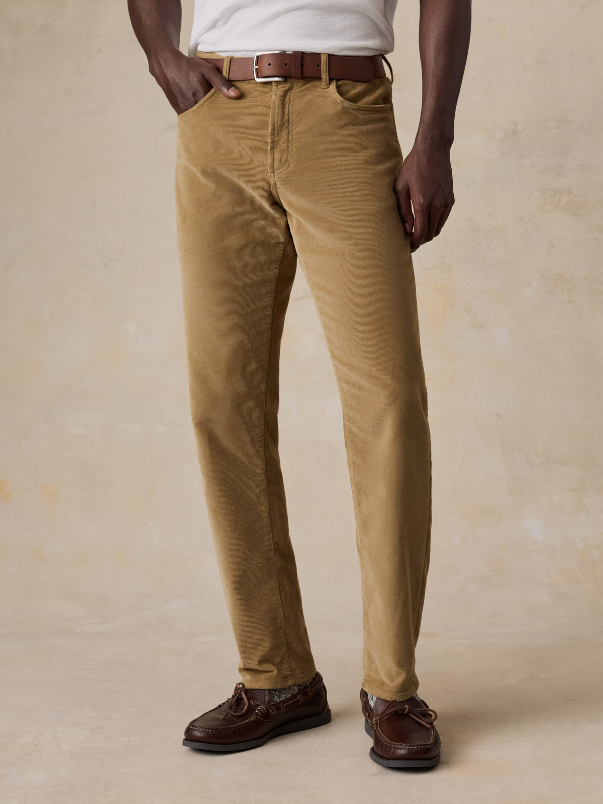 A man wearing a white tee and tan corduroy pants, image 2 of 5