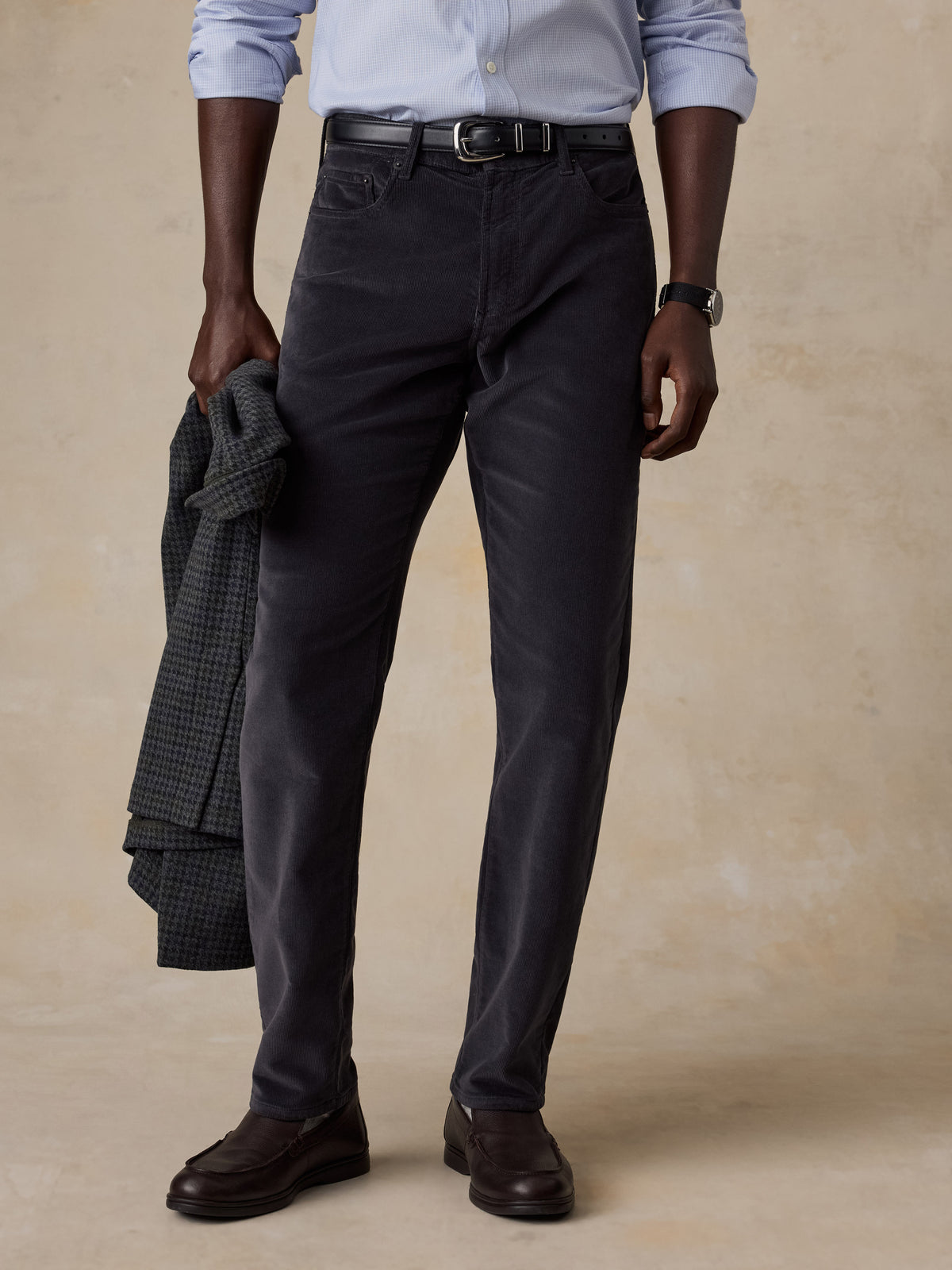 A man wearing a blue button up shirt and grey corduroy pants, image 1 of 5