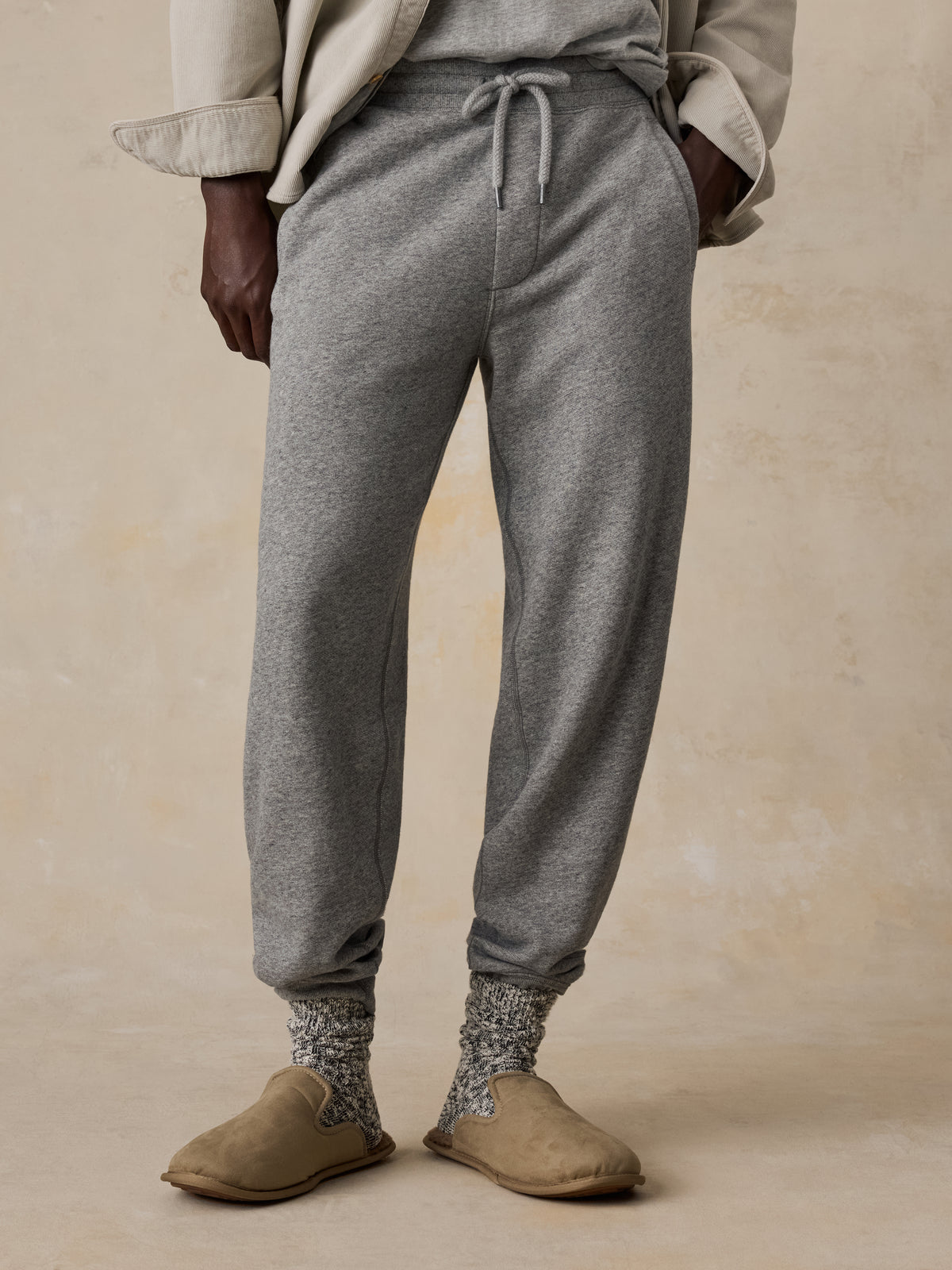 A man wearing grey sweatpants and slippers, image 2 of 5