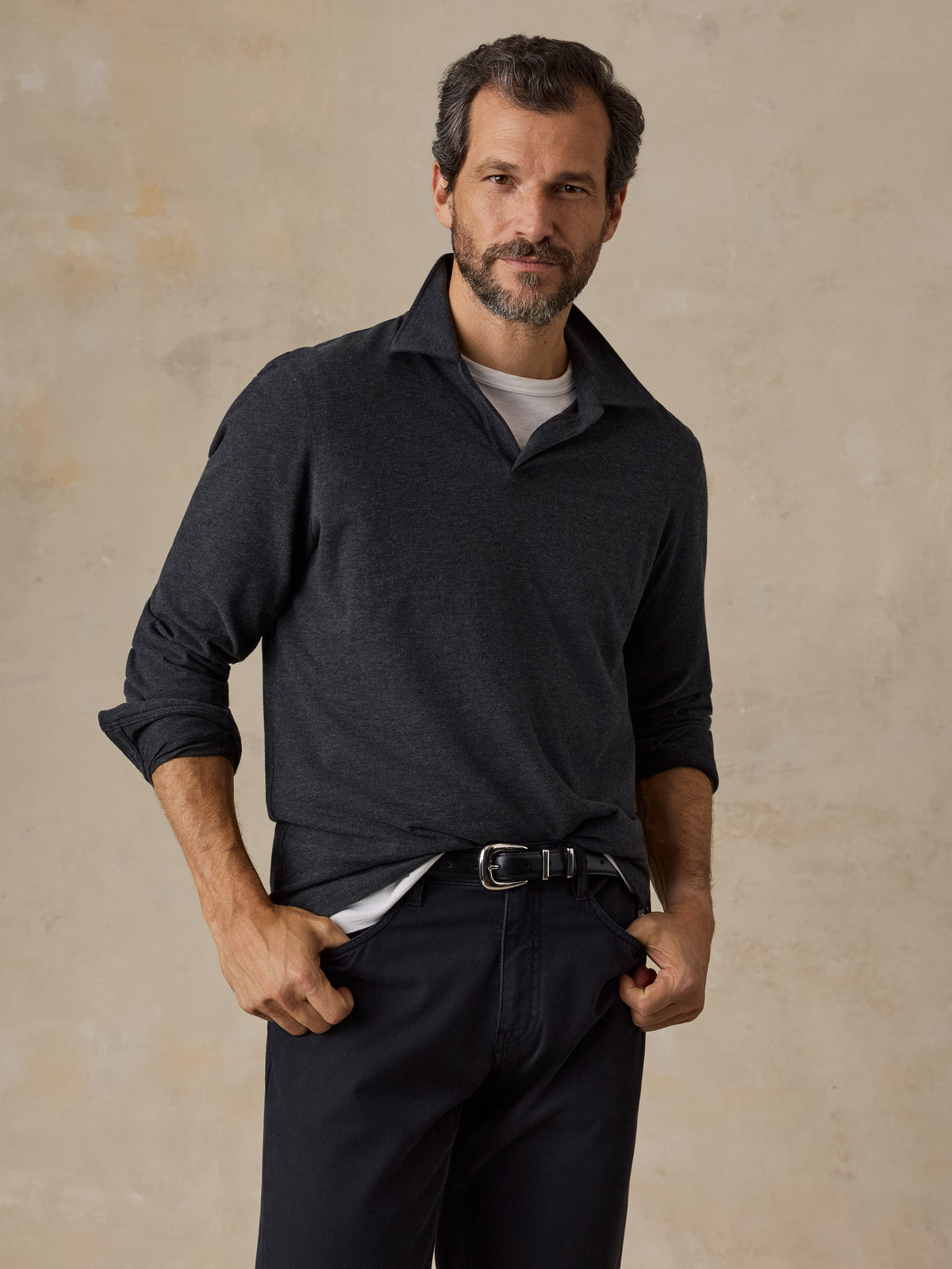 A man wearing a dark grey sweater polo and black chino pants, image 1 of 6