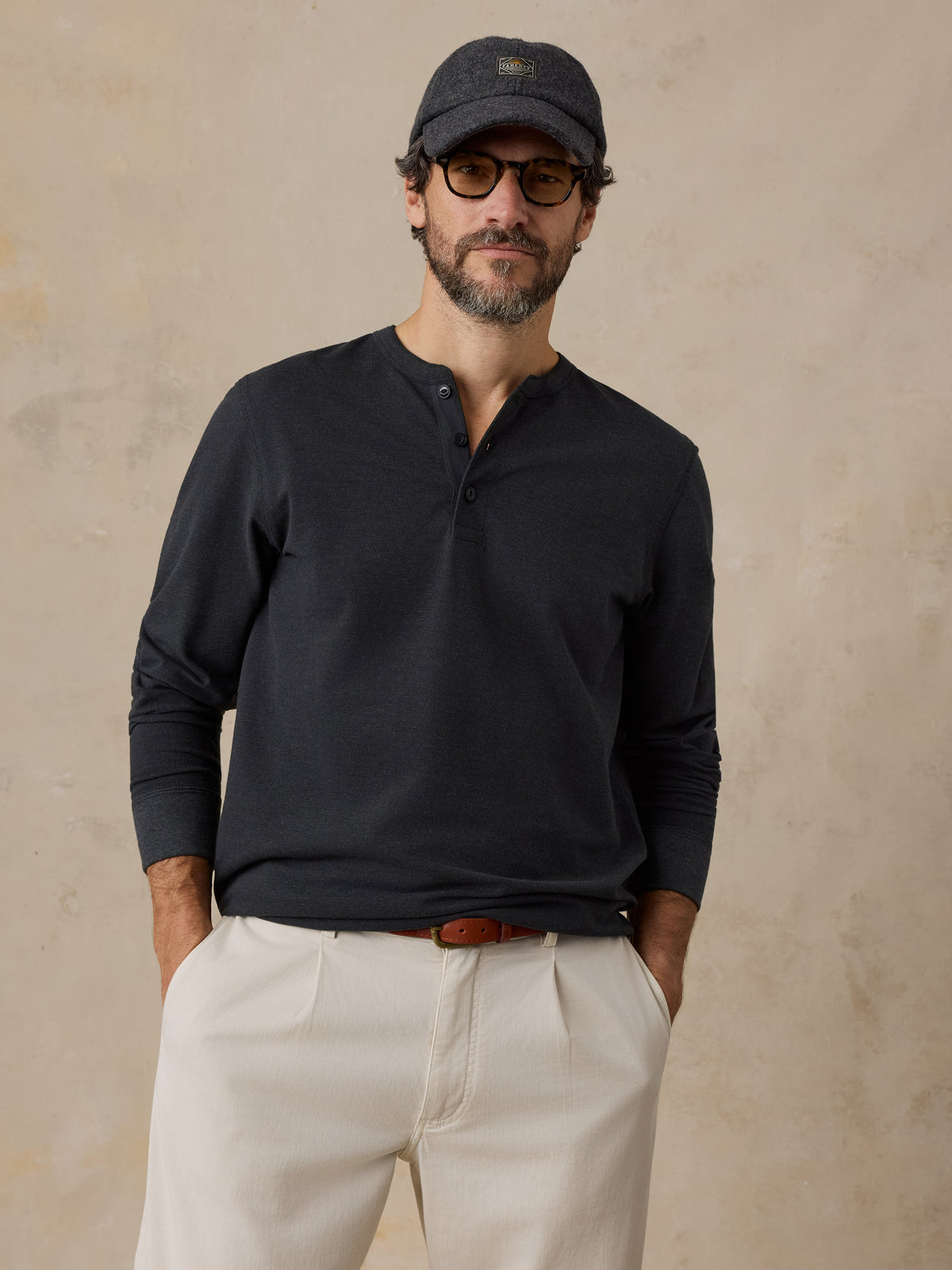A man wearing a black henley and chino pants, image 1 of 6