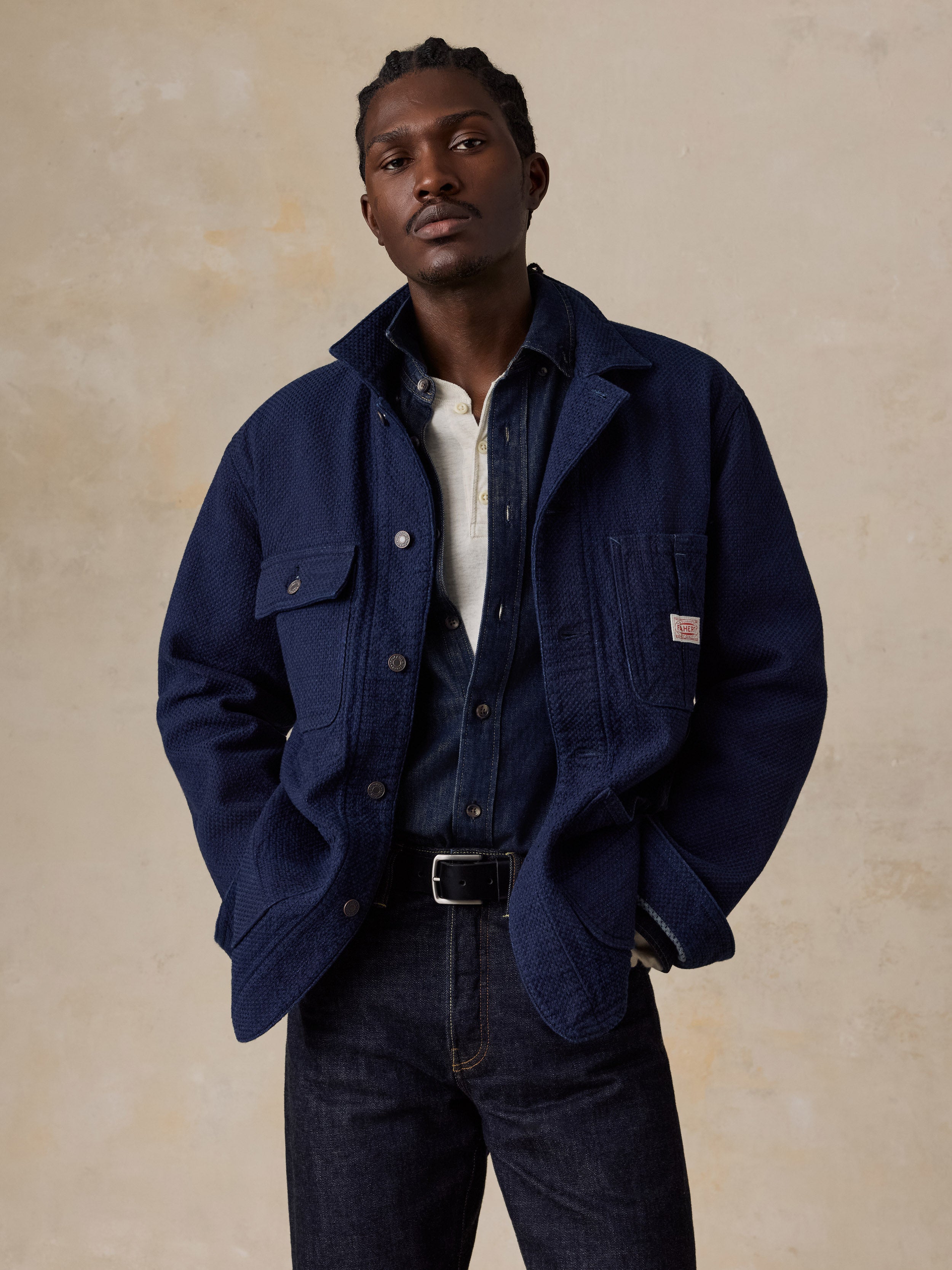 A man wearing a blue jacket over a denim shirt and blue jeans