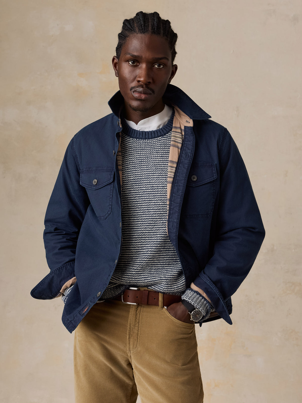A man wearing a blue jacket over a blue striped sweater and tan corduroy pants, image 1 of 5