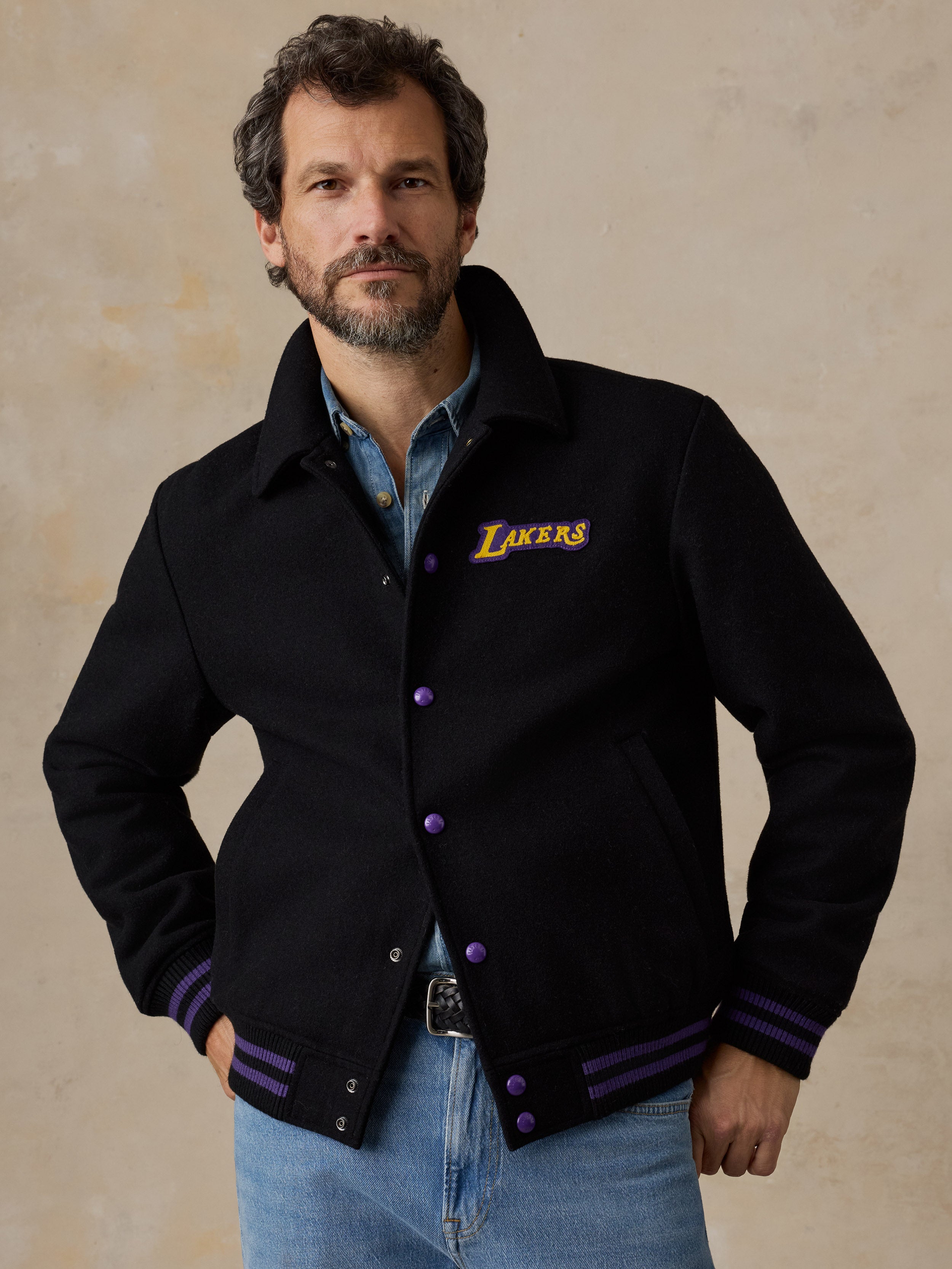 A man wearing a black LA Lakers varsity jacket and blue jeans
