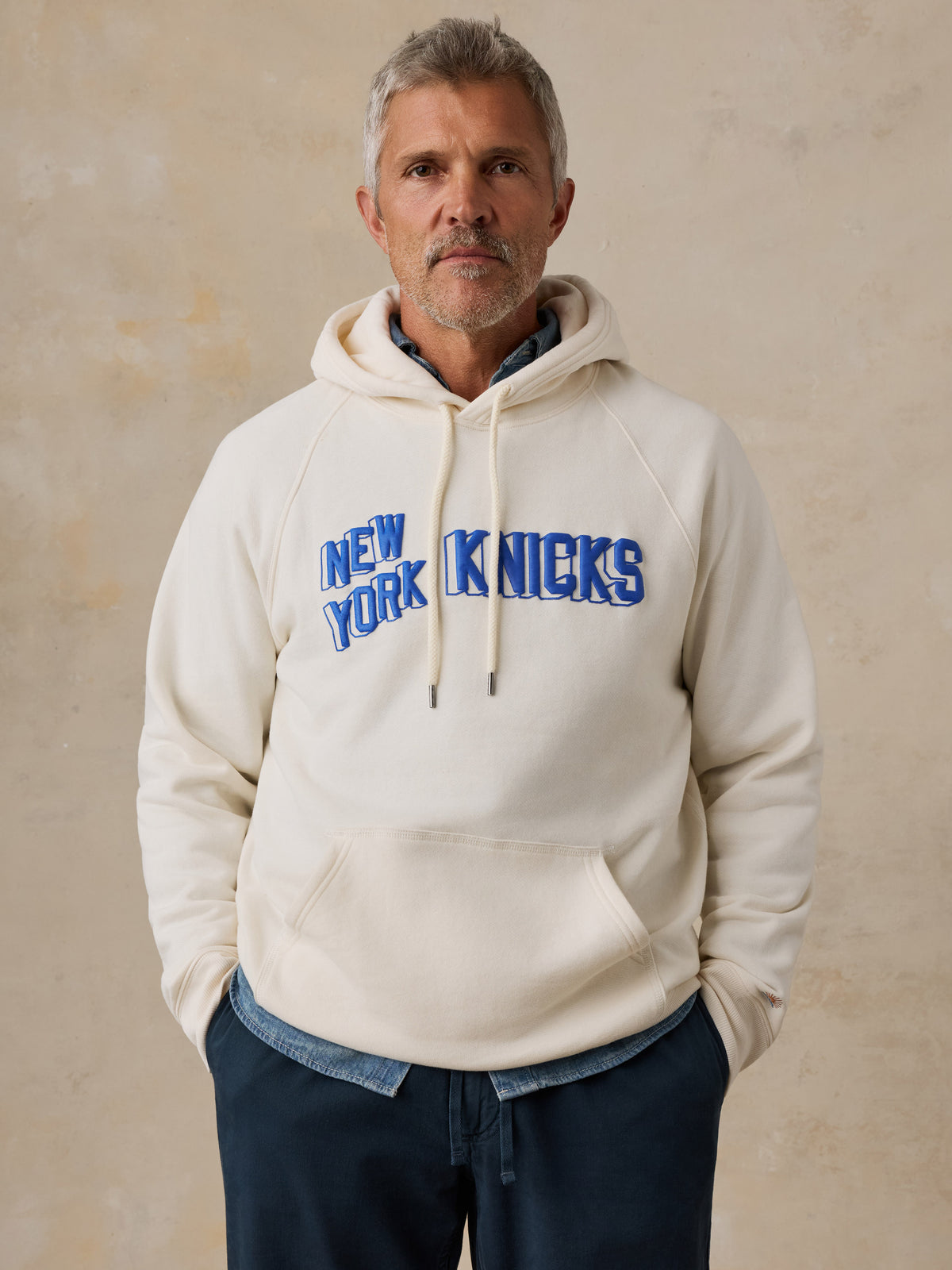 A man wearing a white NY Knicks hoodie, image 1 of 6