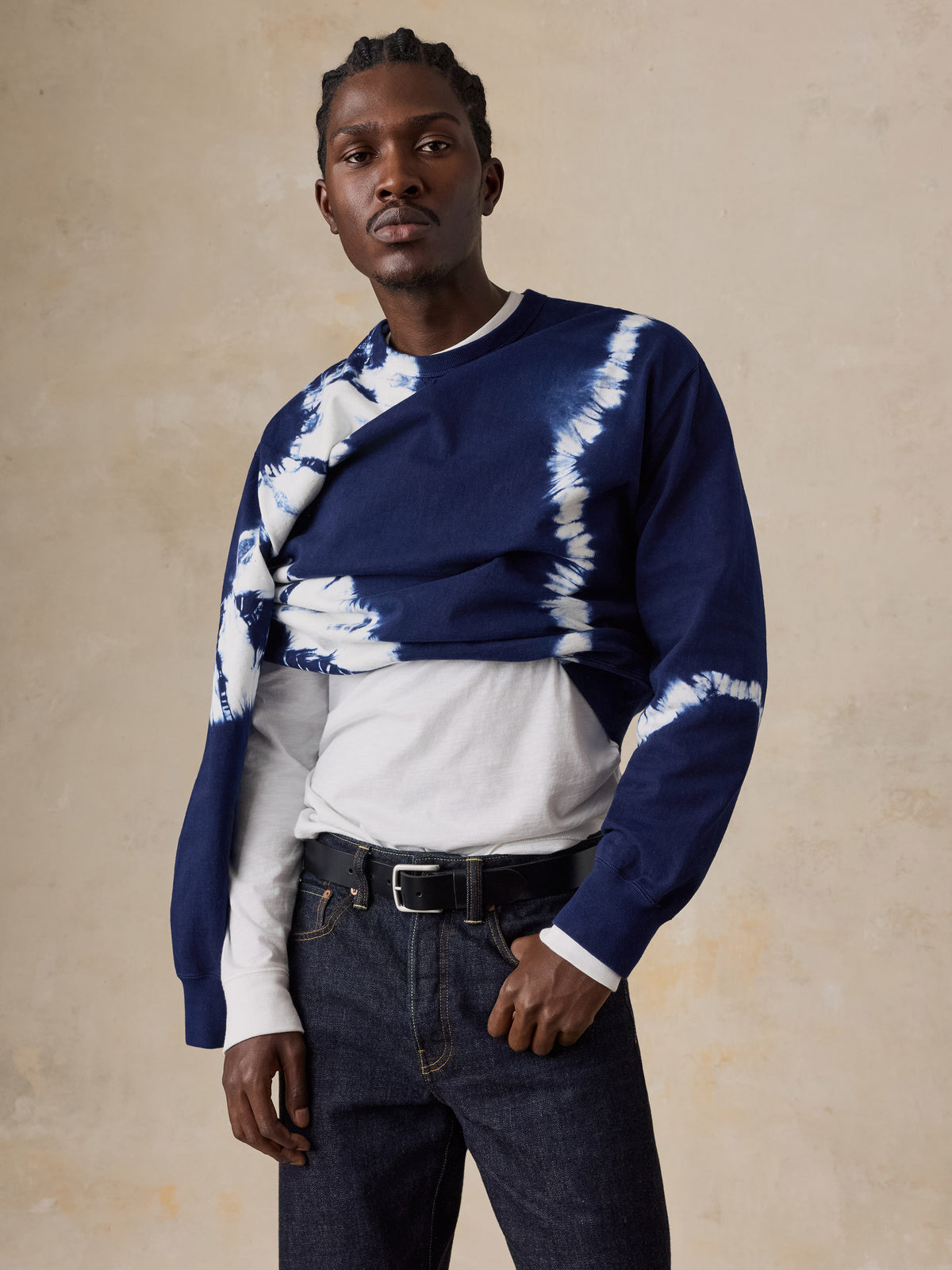 A man wearing a shibori dyed sweatshirt and blue jeans, image 6 of 6
