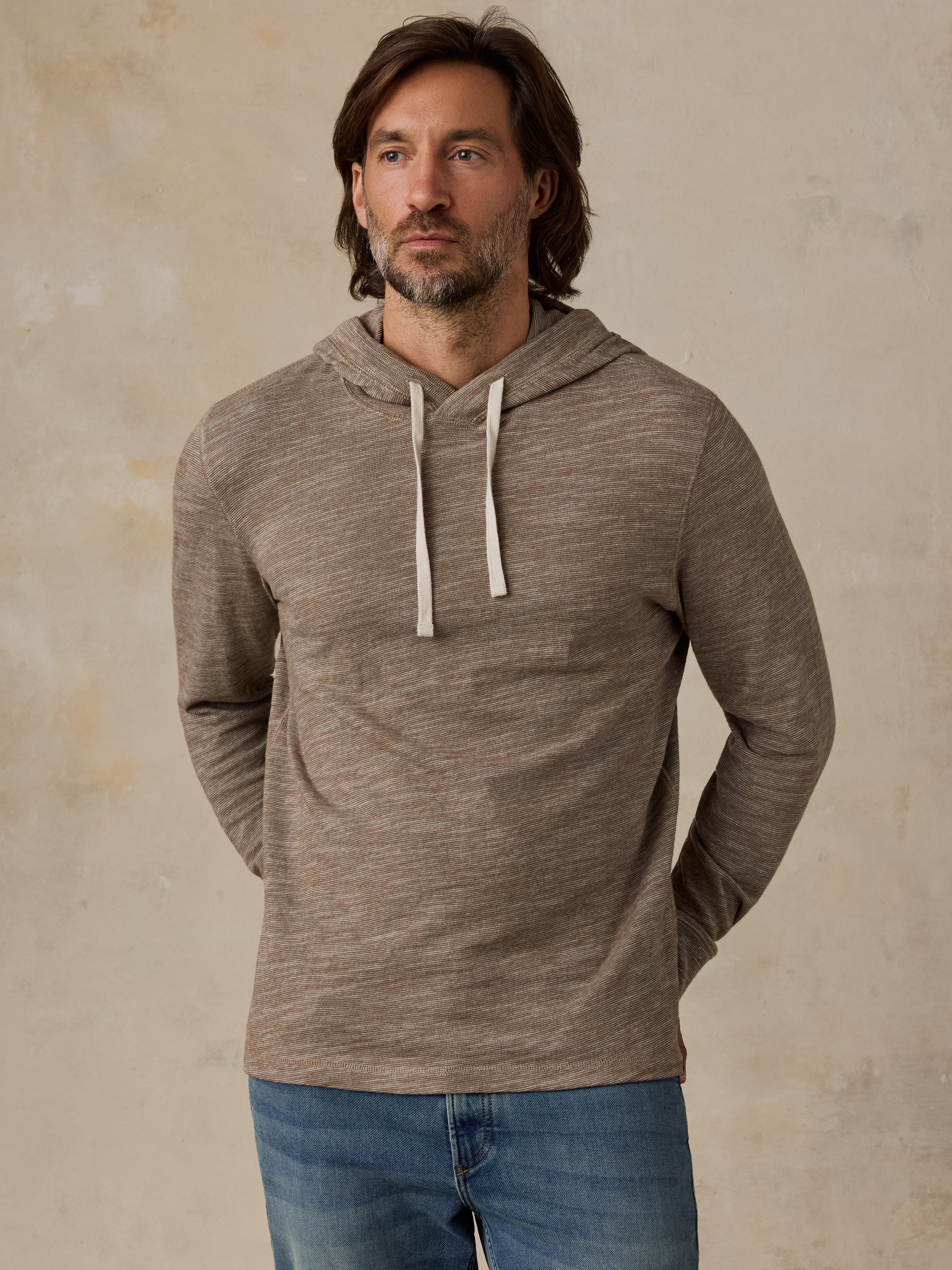 A man wearing a heathered taupe-brown long-sleeve hoodie and blue jeans