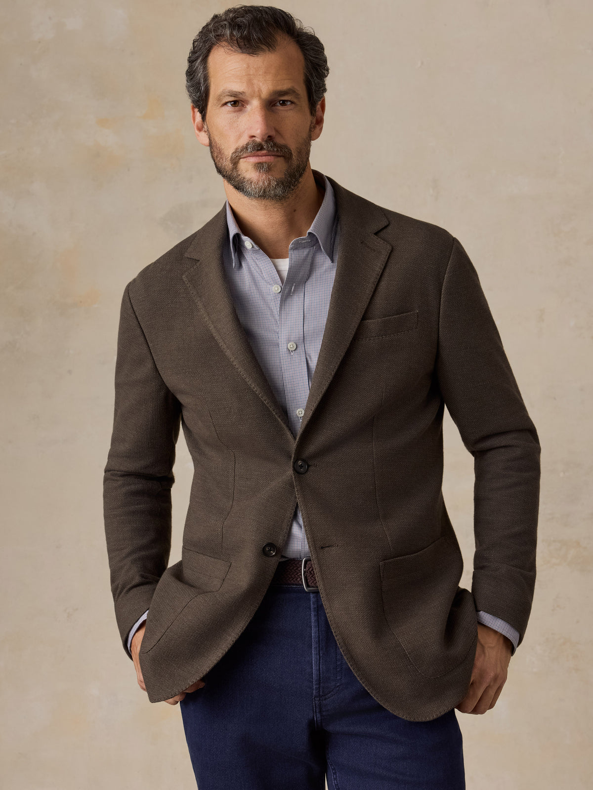 A man wearing a brown blazer over a blue shirt and blue jeans, image 1 of 5