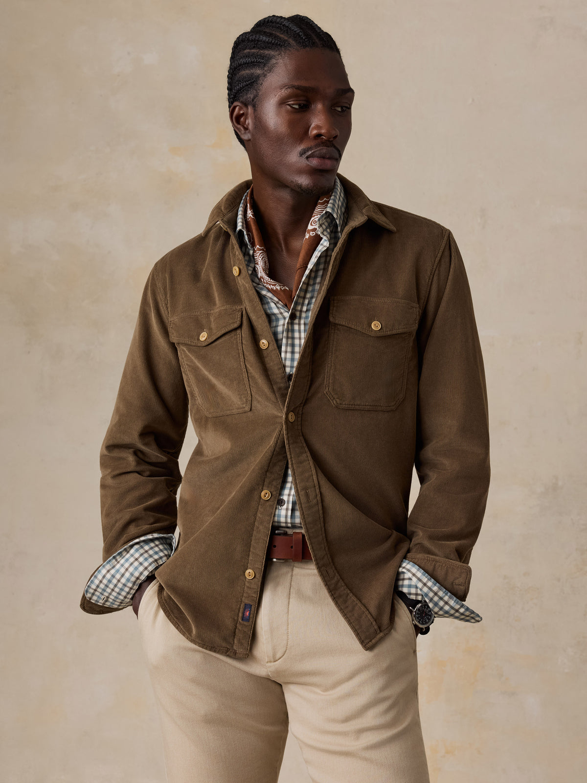 A man wearing a brown corduroy shirt over a plaid button down and beige pants, image 4 of 6