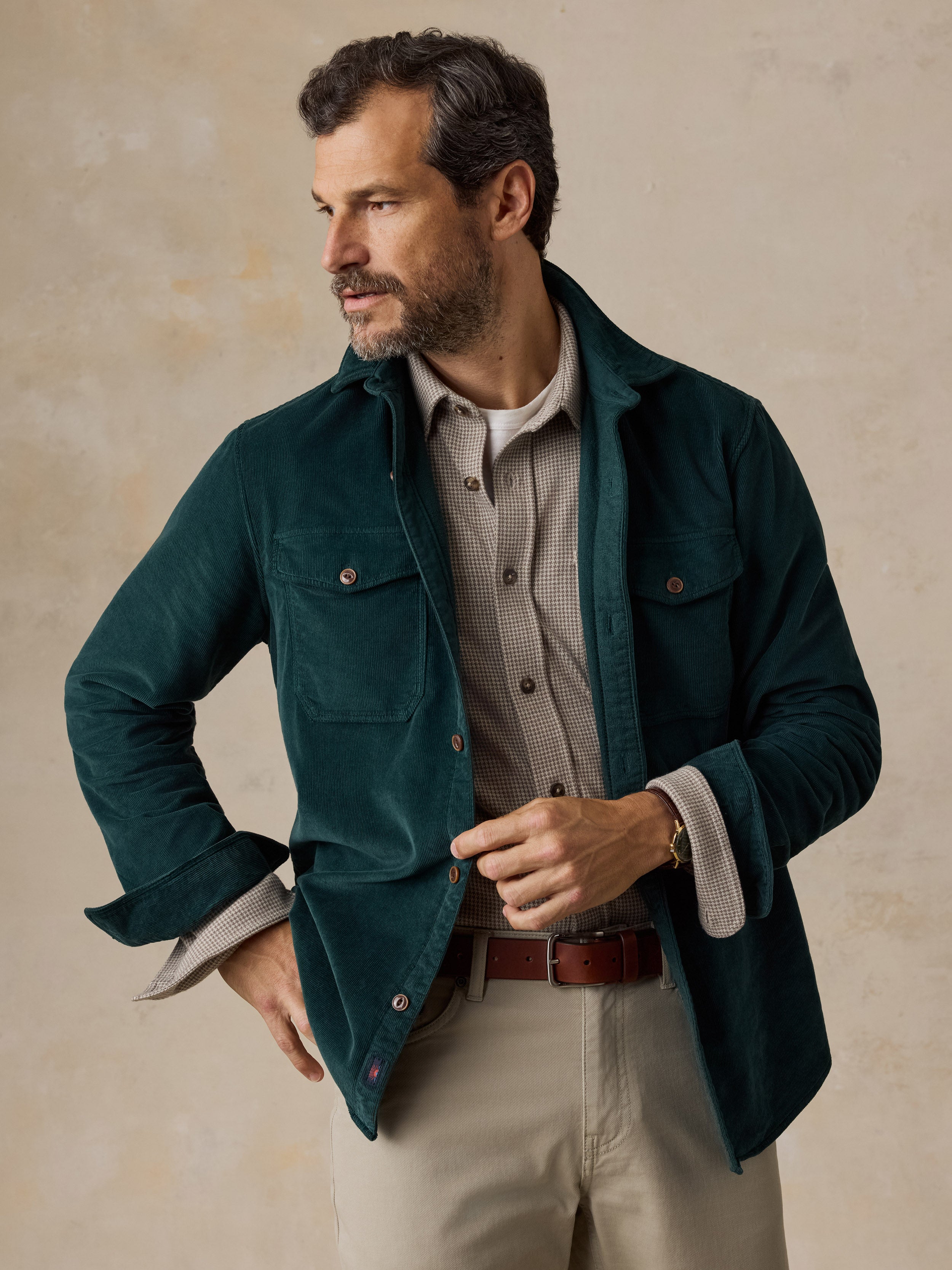 A man wearing a green overshirt, a beige check shirt, and beige pants