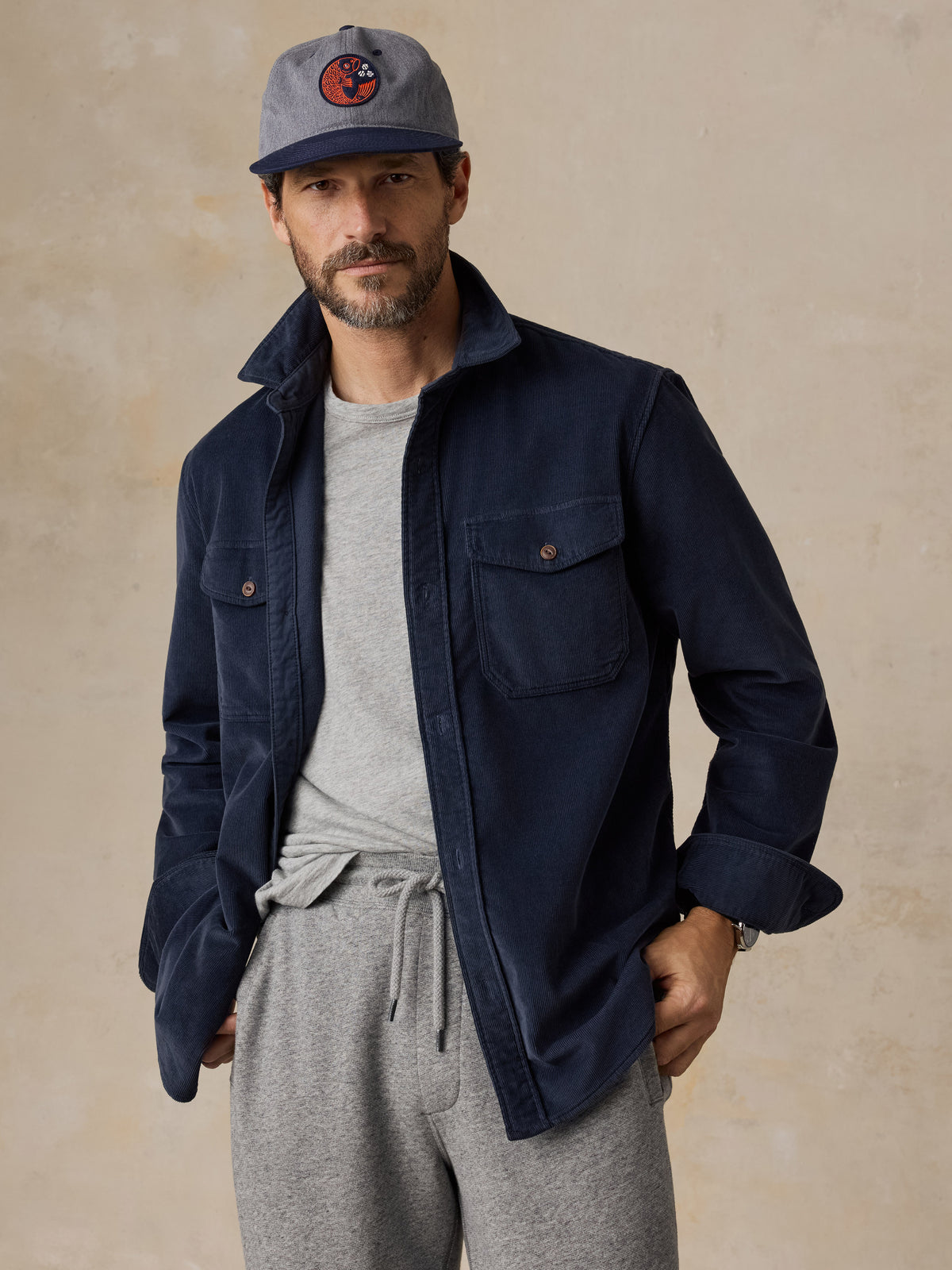 A man wearing a navy blue overshirt with a grey tee and sweatpants, image 1 of 6