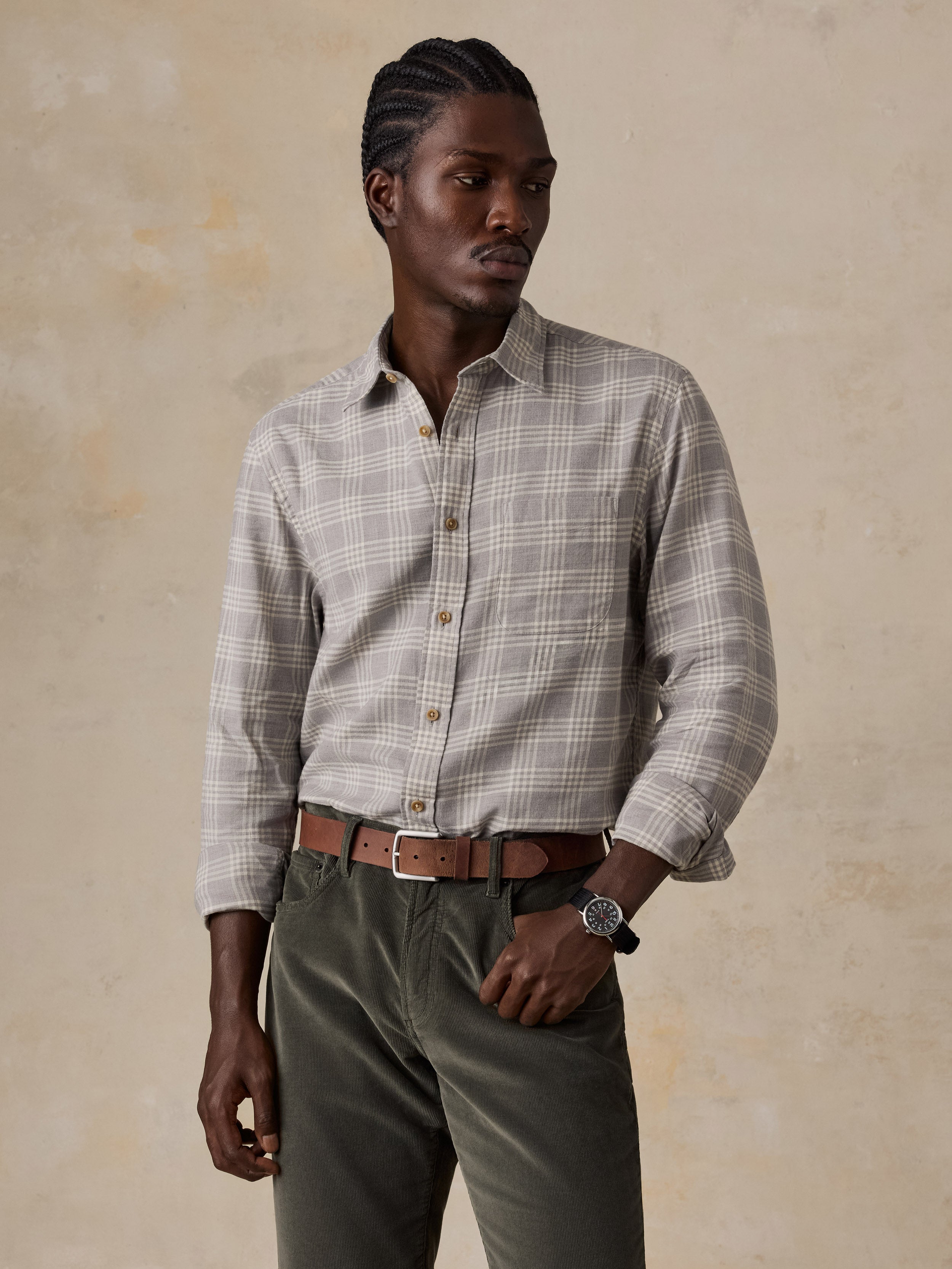 A man wearing a grey plaid button up shirt and green corduroy pants