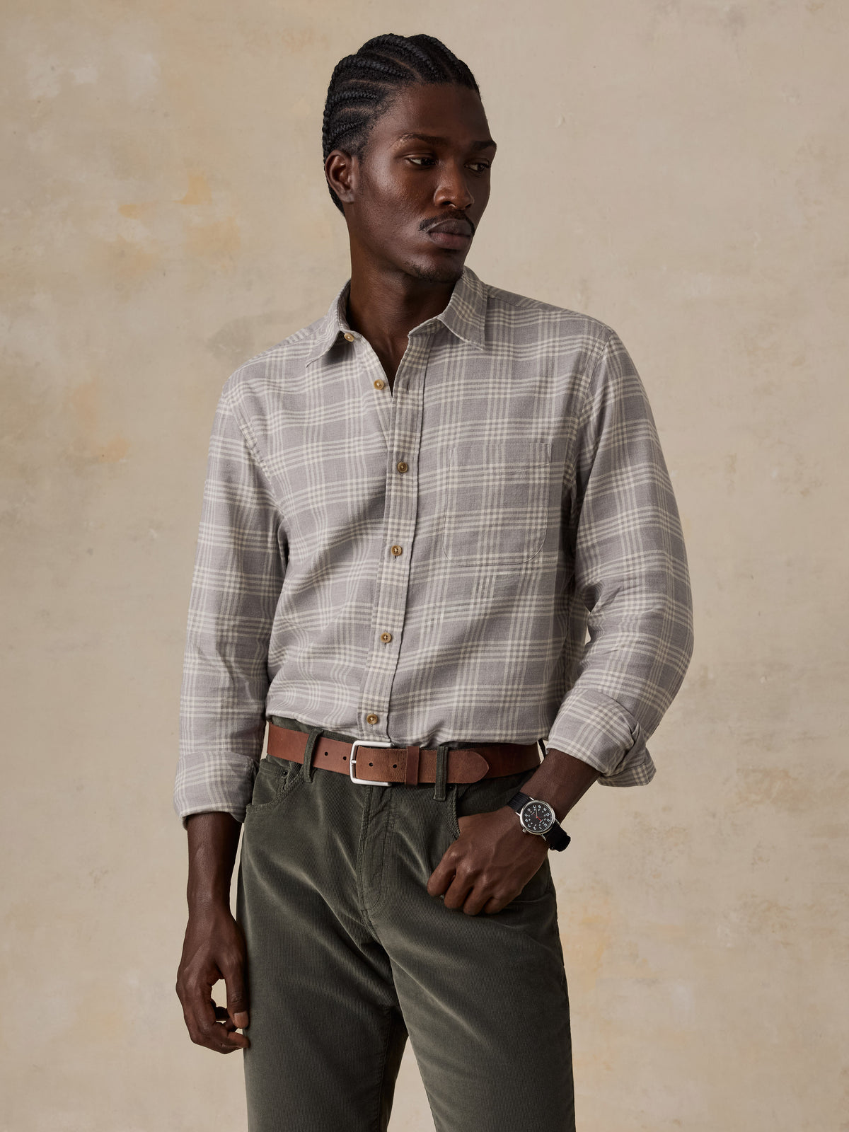 A man wearing a grey plaid button up shirt and green corduroy pants, image 1 of 5