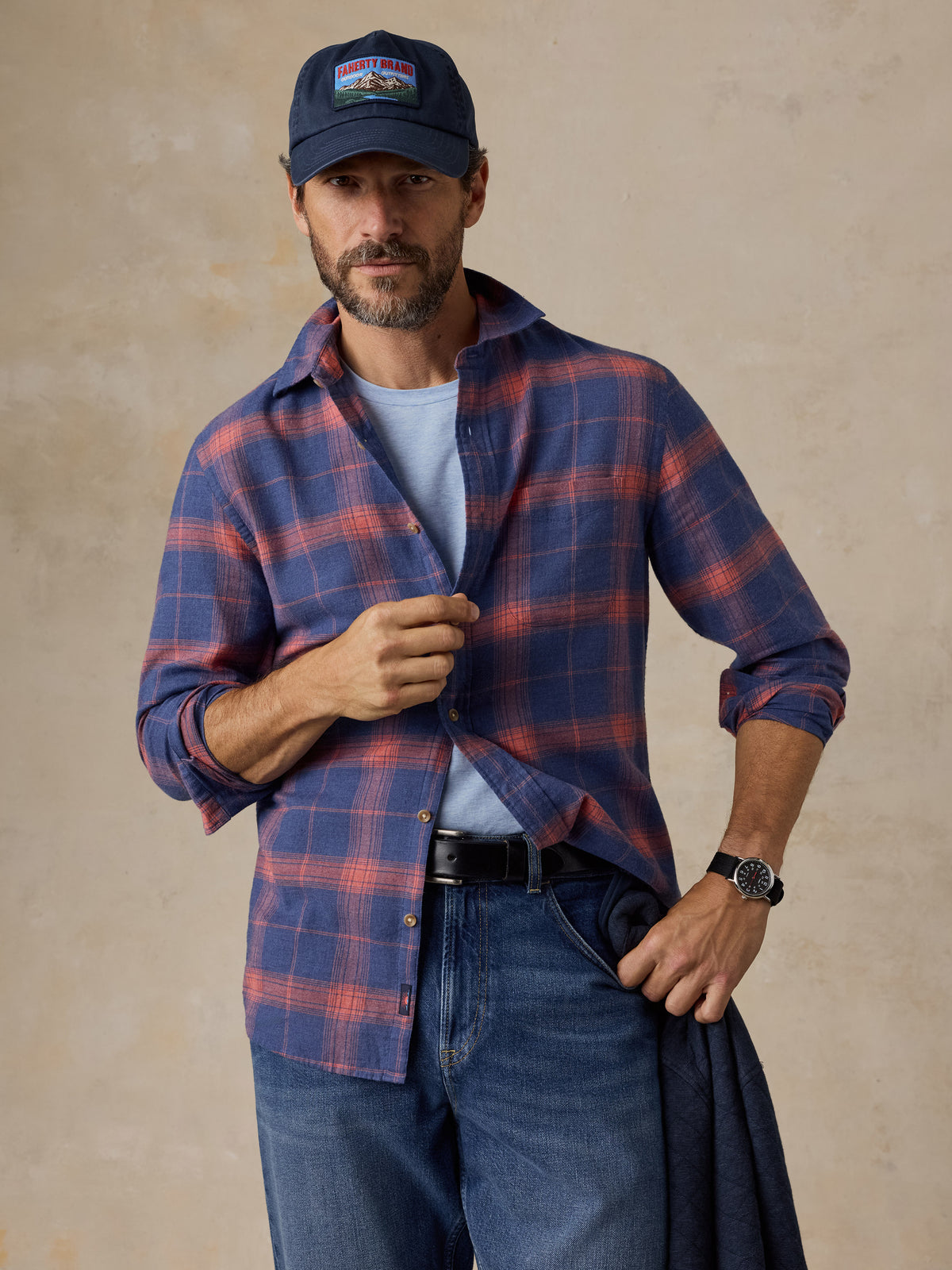 A man wearing a blue plaid shirt, blue jeans, and a hat, image 1 of 5