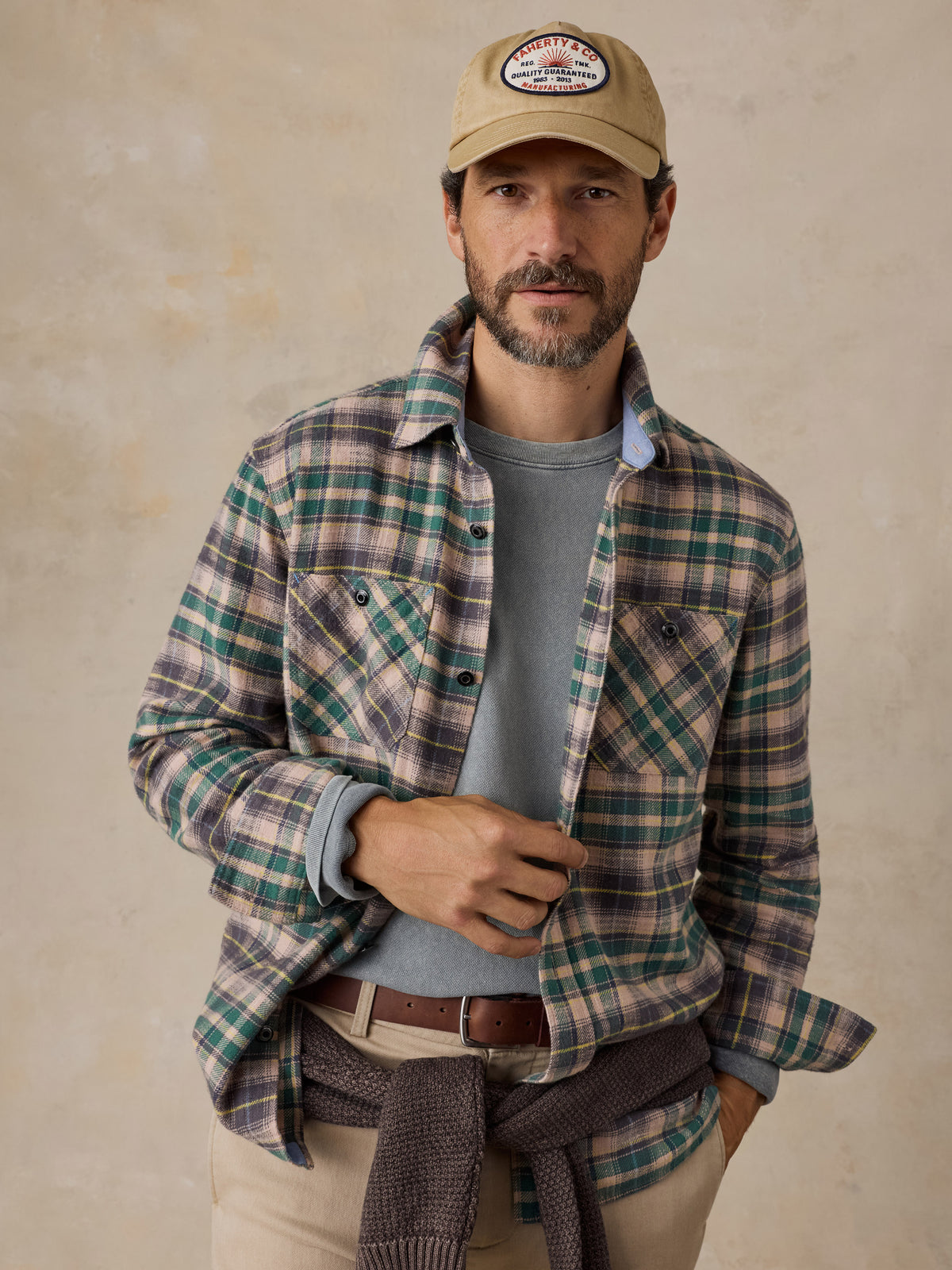 A man wearing a green flannel over a green shirt with beige pants and a hat, image 1 of 5