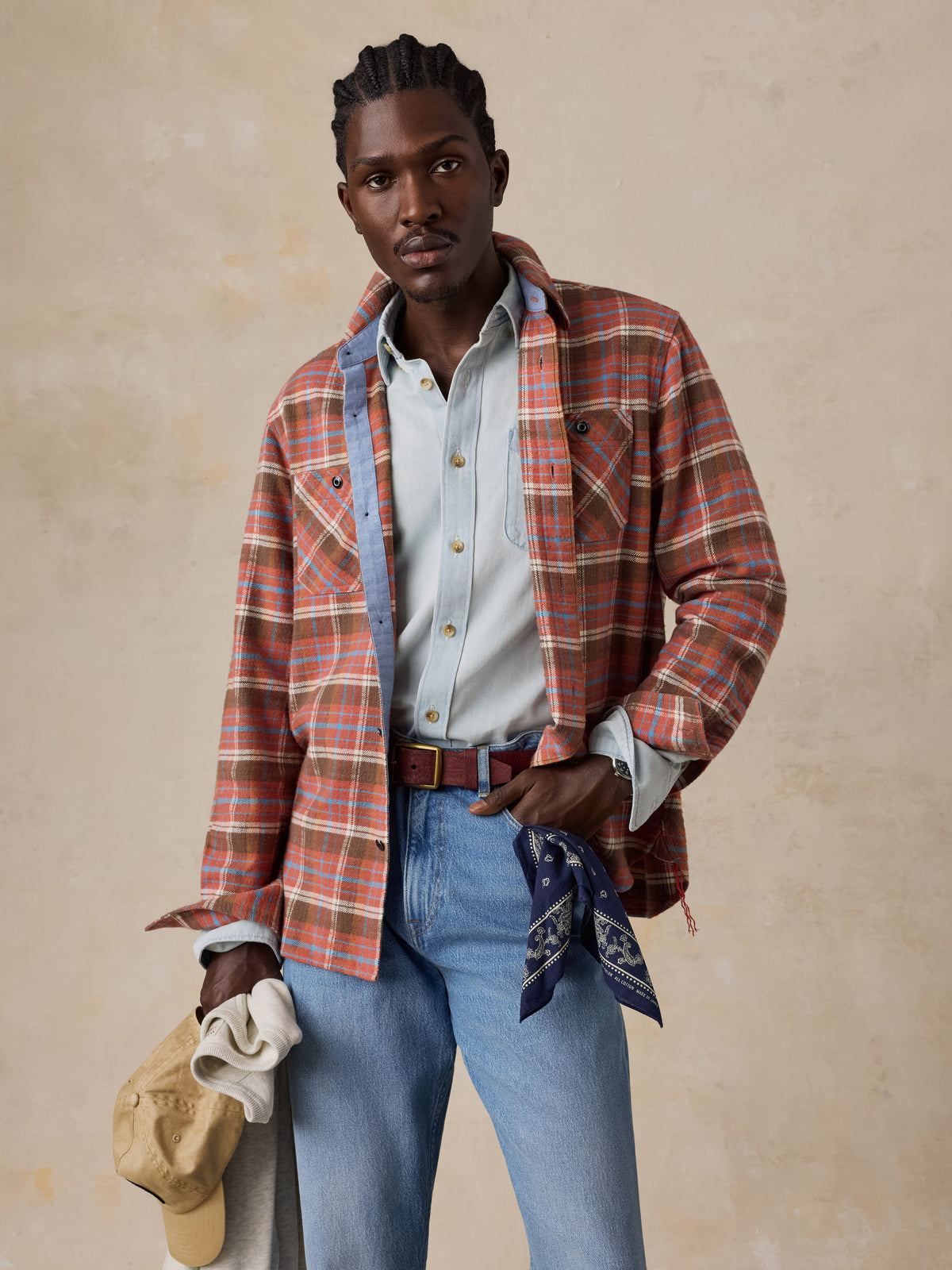A man wearing a red plaid flannel over a chambray shirt and blue jeans, image 1 of 5