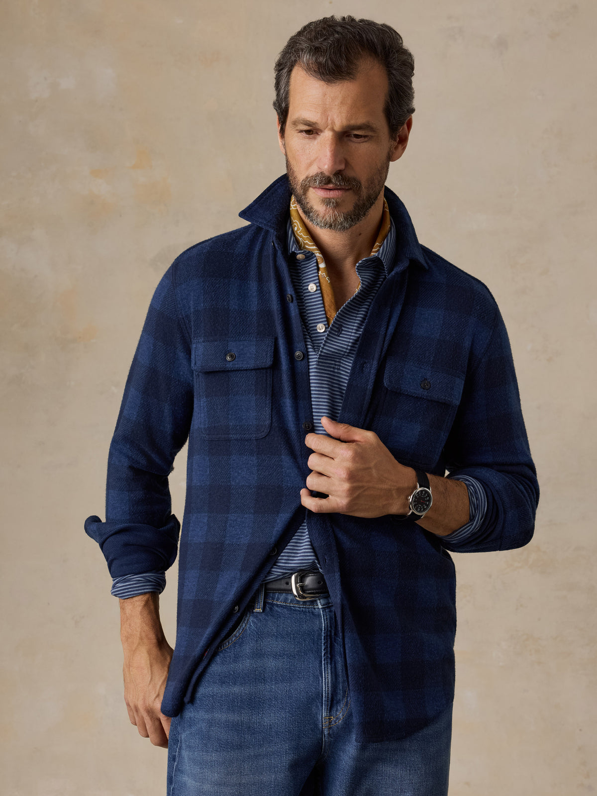 A man wearing a blue checkered flannel and blue jeans, image 1 of 5