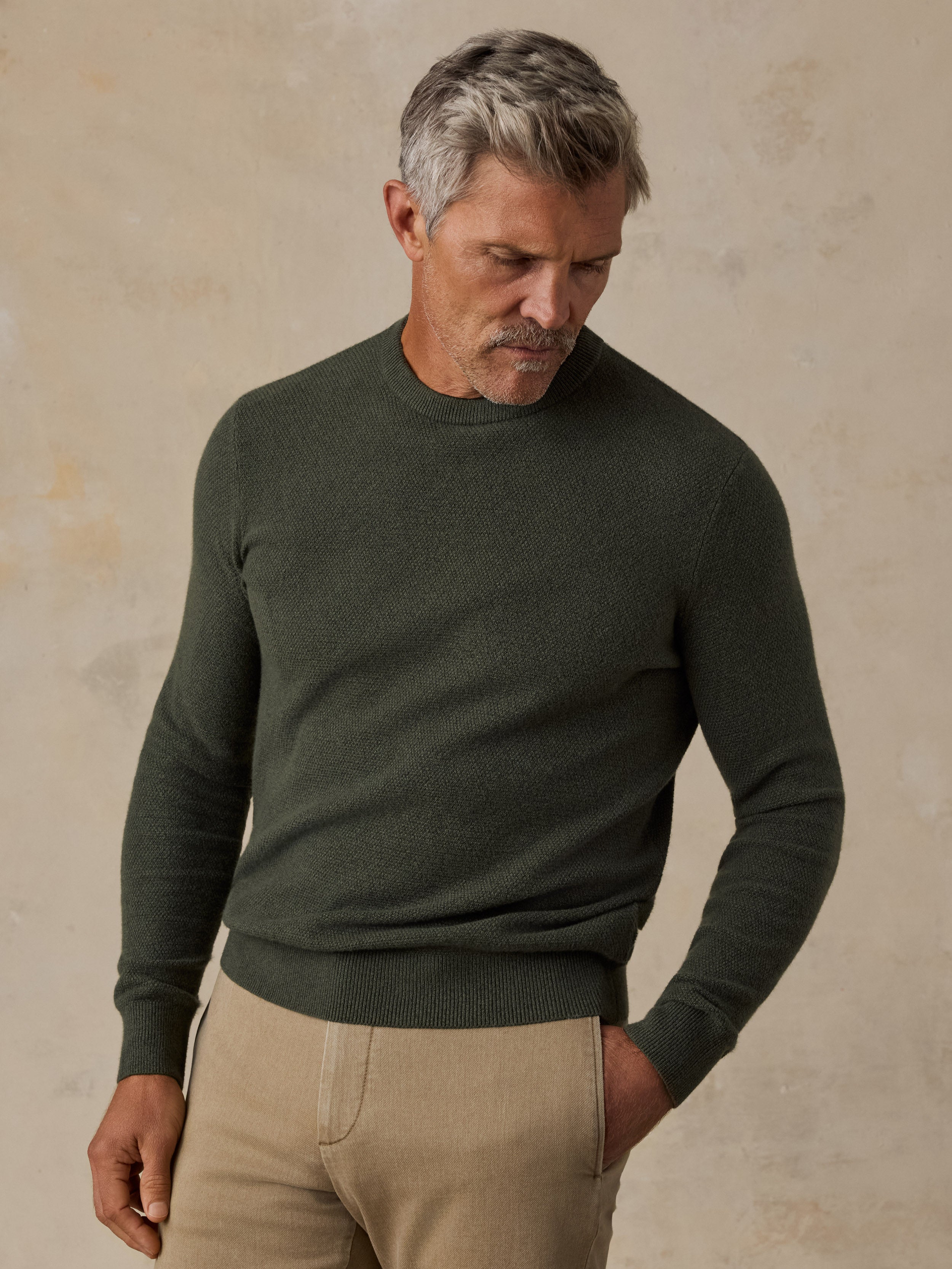 A man wearing a dark green sweater and beige pants