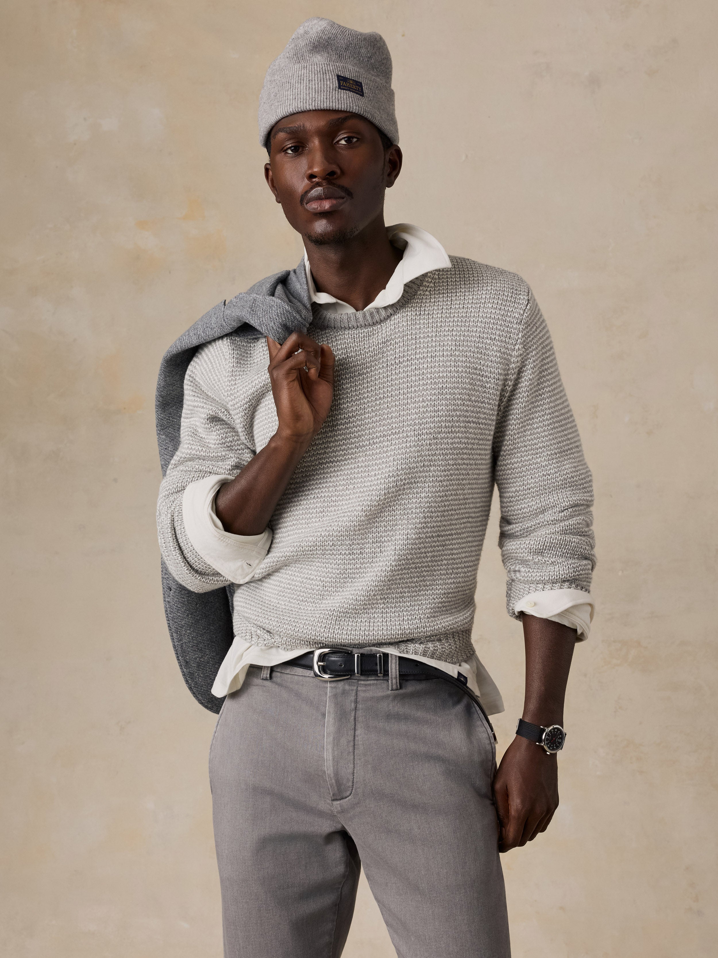 Man wearing a light grey sweater over a white shirt and grey pants