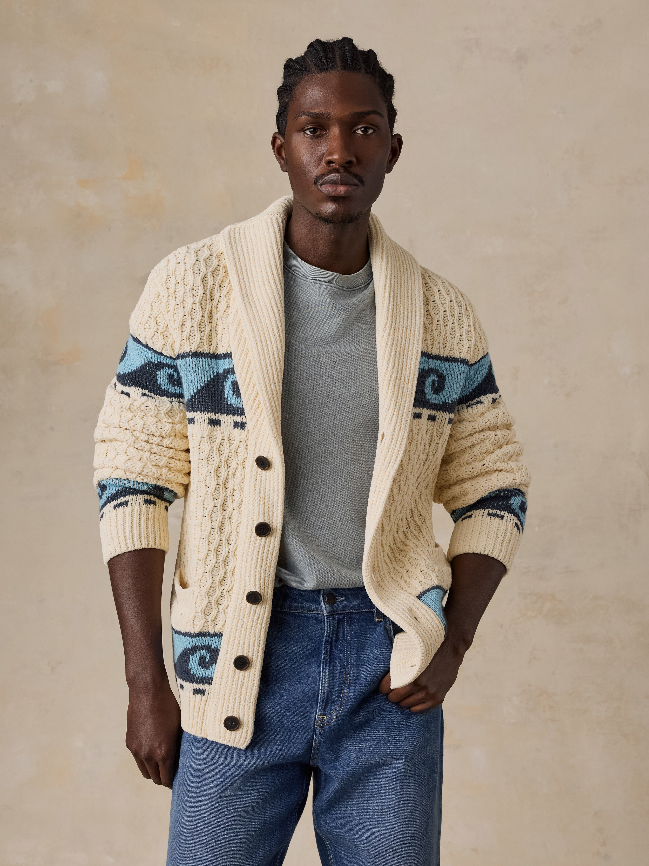A man wearing a cream and blue printed cardigan with blue jeans