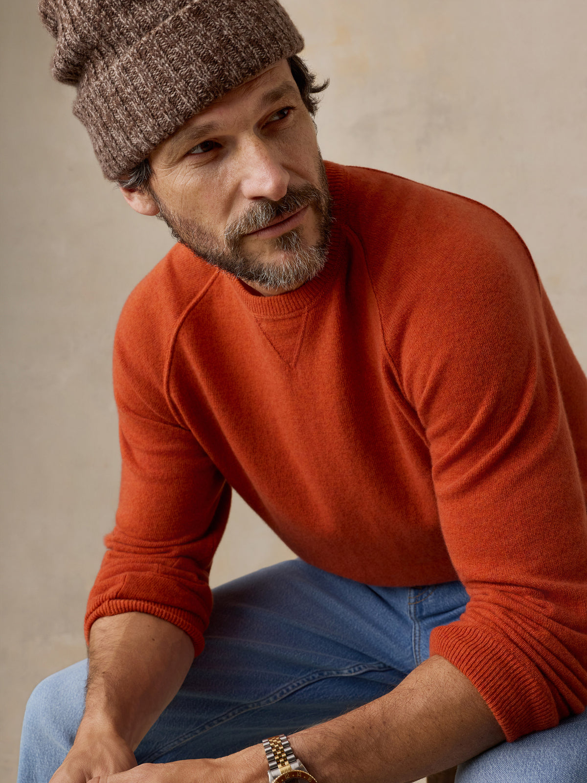 Close up of a man wearing an orange sweater and a beanie, image 3 of 6