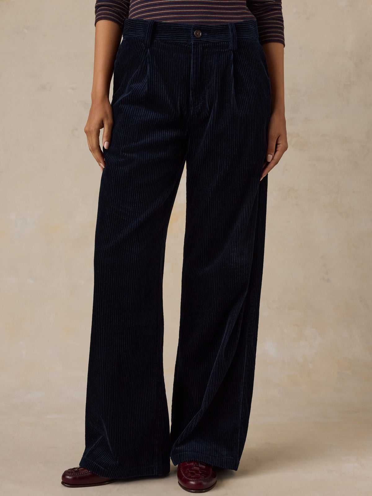 A woman wearing dark navy blue corduroy pants and a striped top, image 2 of 7
