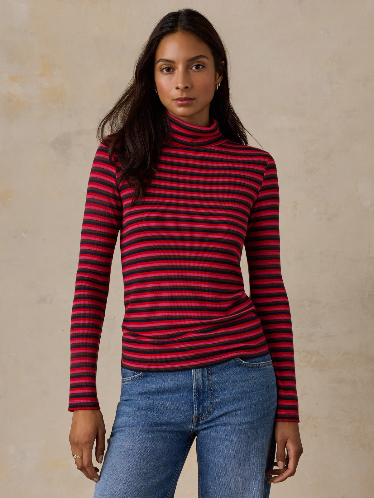 A woman wearing a red striped turtleneck and jeans, image 1 of 6