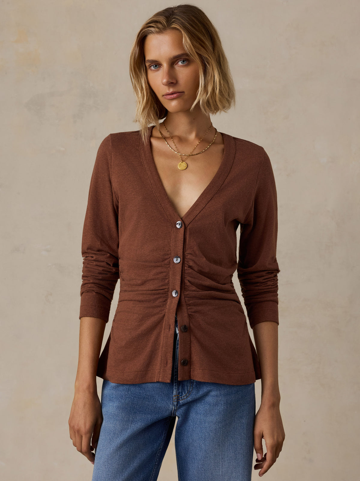 A woman wearing a brown long sleeve top and blue jeans, image 1 of 6