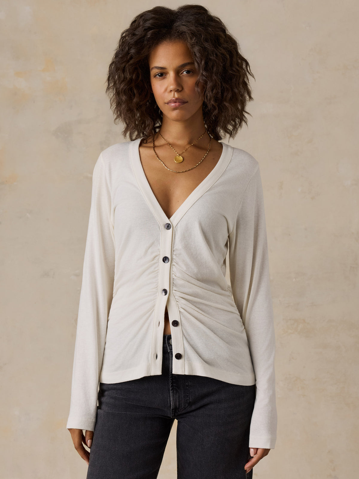 A woman wearing a white cardigan and black jeans, image 1 of 6