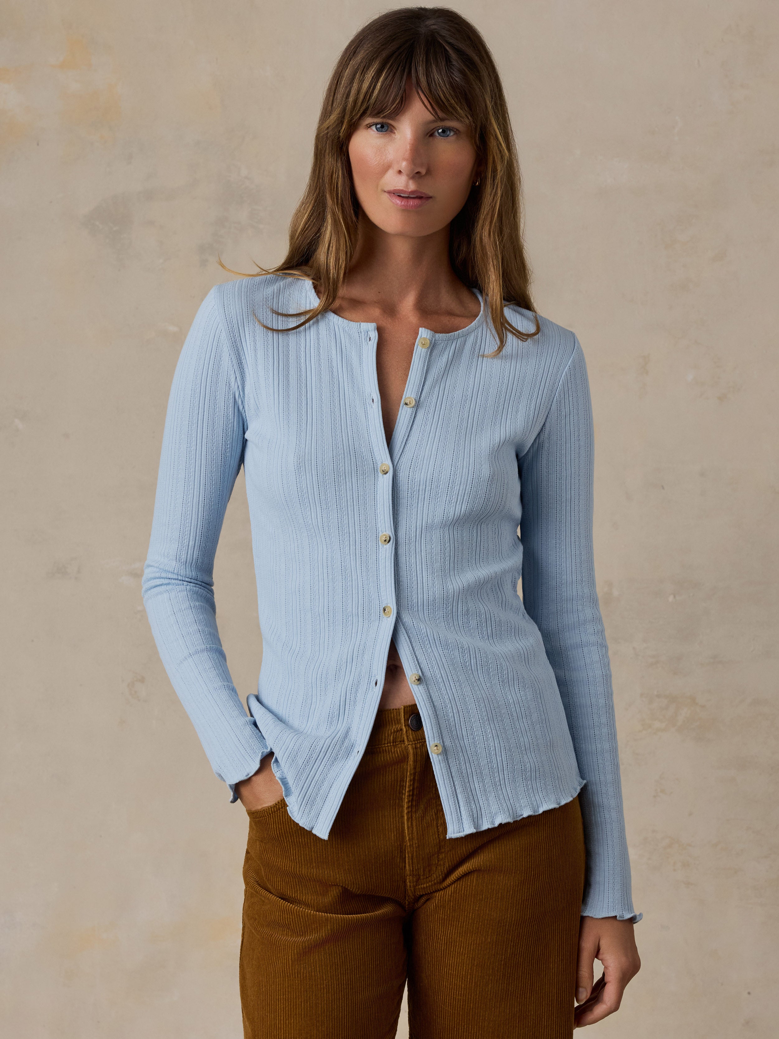 A woman wearing a light blue cardigan and brown corduroy pants