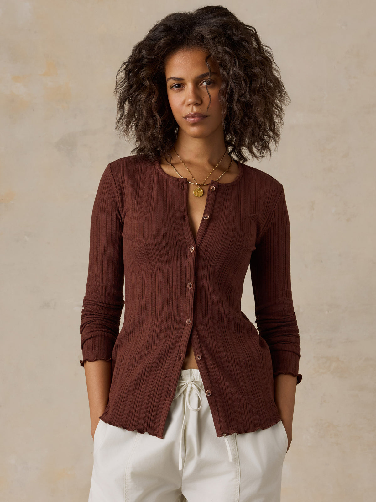 A woman wearing a brown knit cardigan and white pants, image 1 of 6