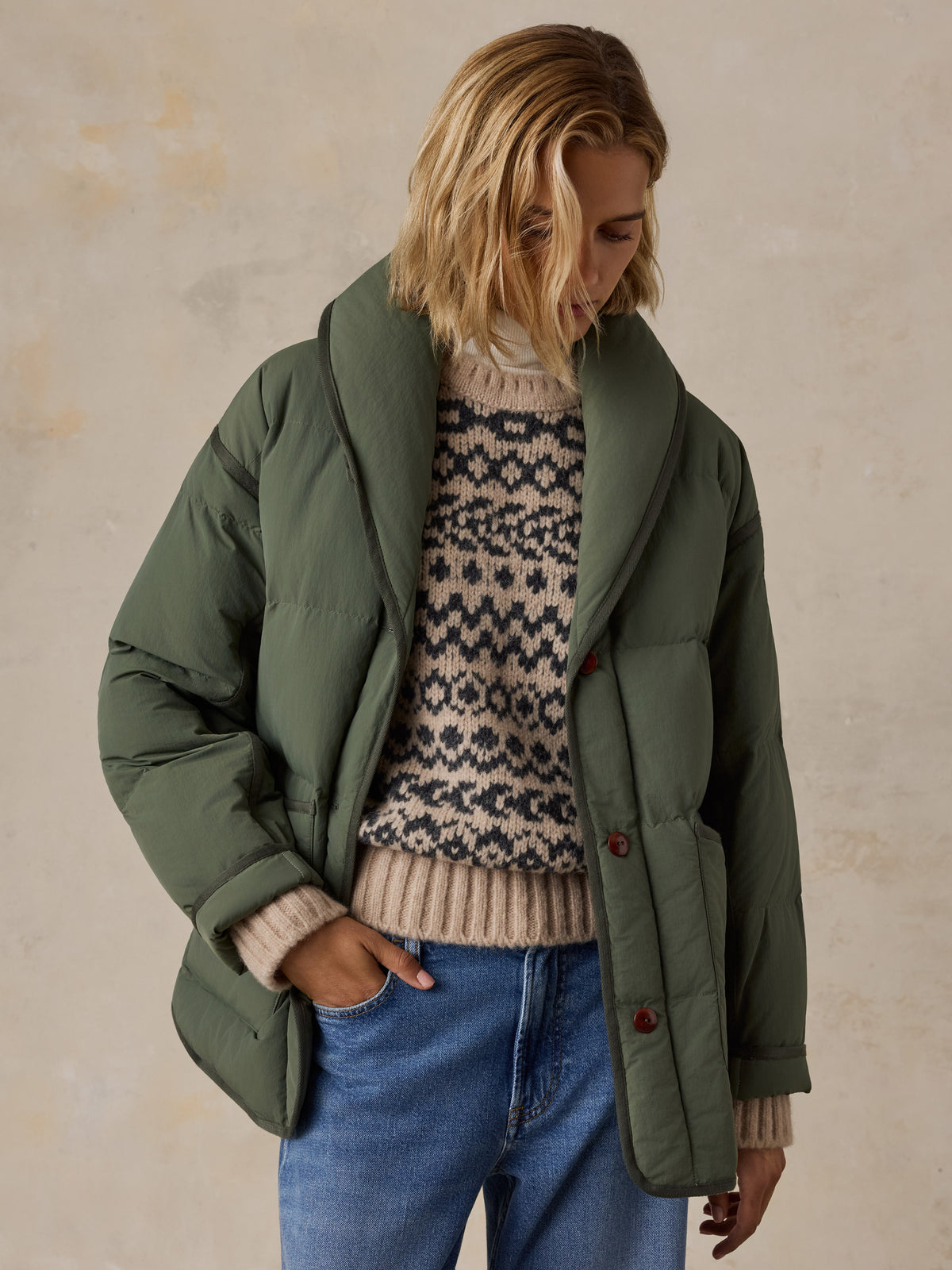 A woman wearing a green jacket over a knit sweater and blue jeans, image 3 of 7