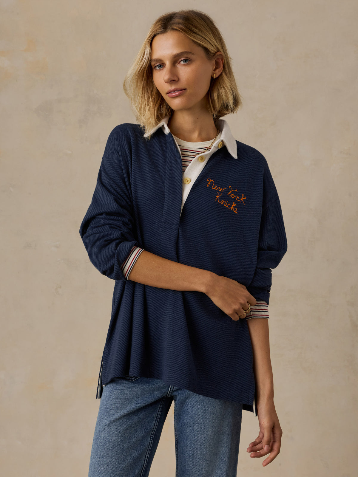 A woman wearing a navy NY Knicks rugby and blue jeans, image 1 of 6