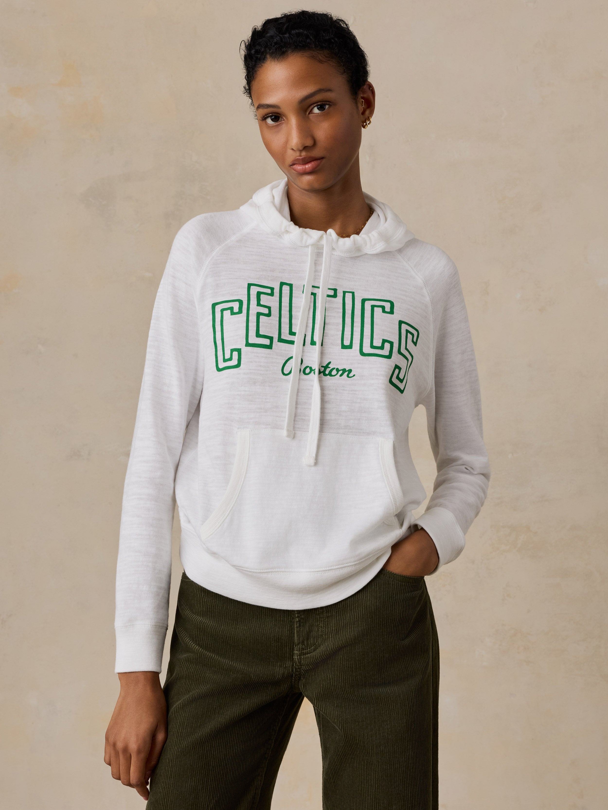 A woman wearing a white Boston Celtics hoodie and green pants