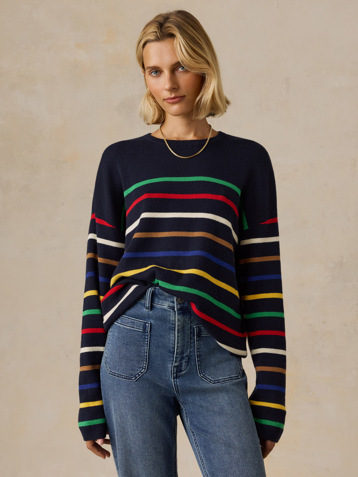 A woman wearing a colorful striped sweater and jeans, image 1 of 5