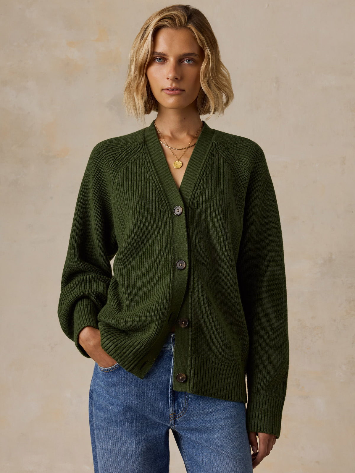 A woman wearing an olive green ribbed knit cardigan with brown buttons, paired with blue jeans, image 1 of 6