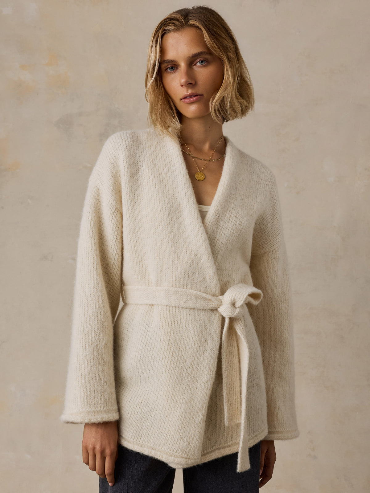 A woman wearing a cream wrap cardigan and black jeans, image 1 of 8