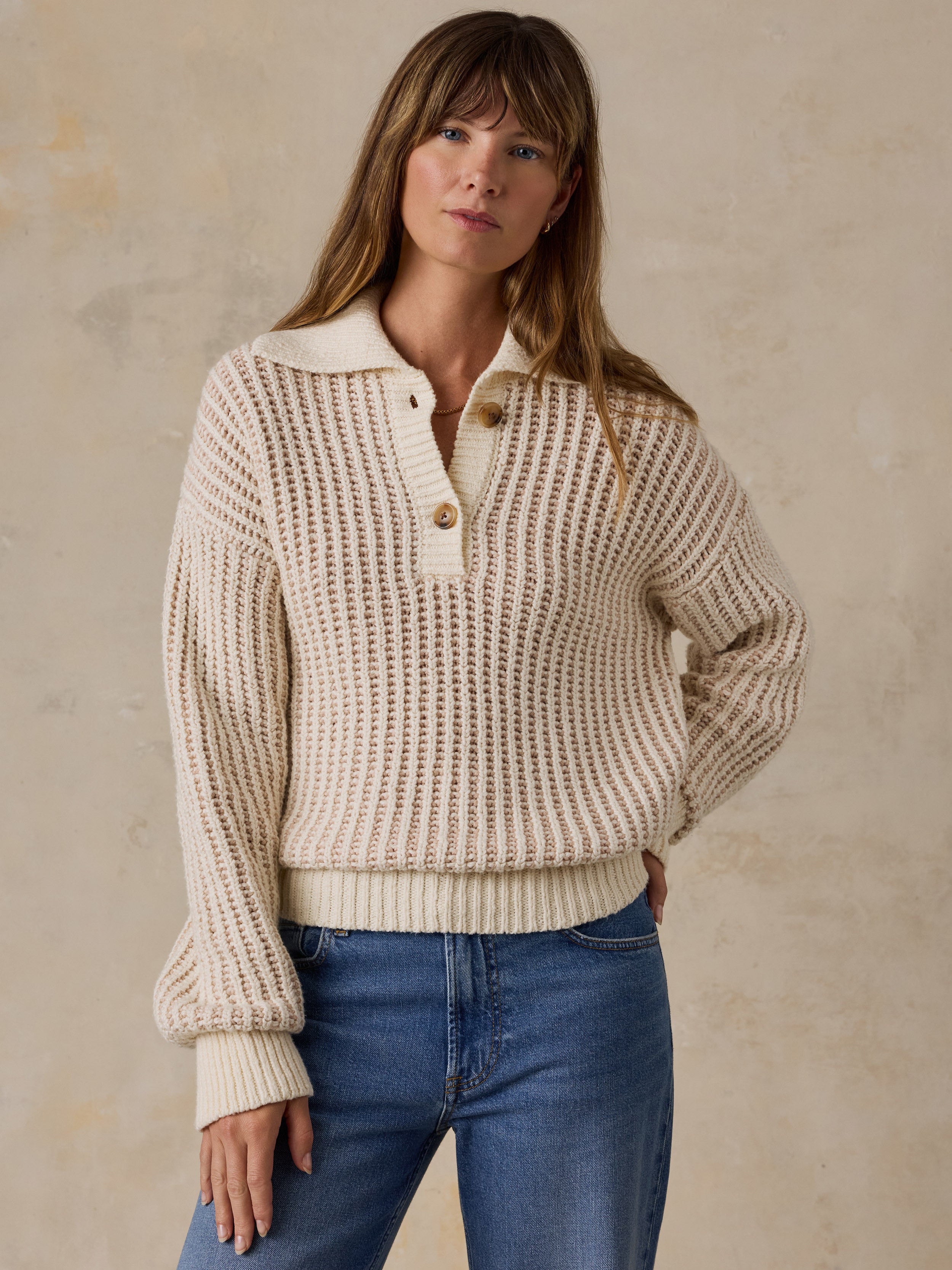 A woman wearing a cream-colored waffle-knit polo sweater and blue jeans