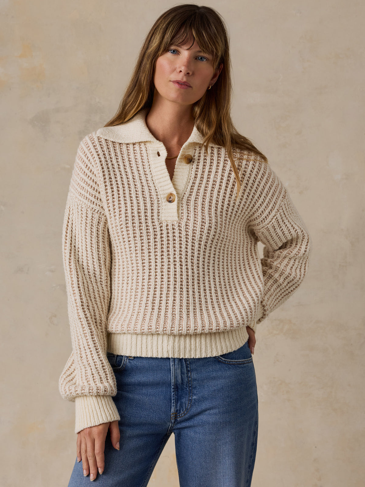 A woman wearing a cream-colored waffle-knit polo sweater and blue jeans, image 1 of 5